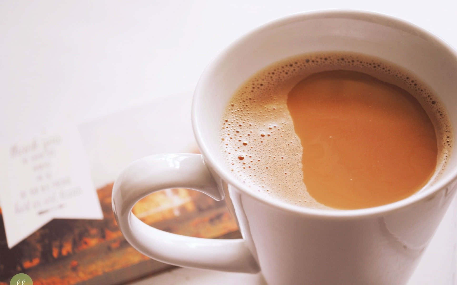 tea 桌布 壁紙 — 一個白色馬克杯的特寫，裝滿了冒煙的咖啡和泡沫，旁邊有一張感謝卡和一本書。