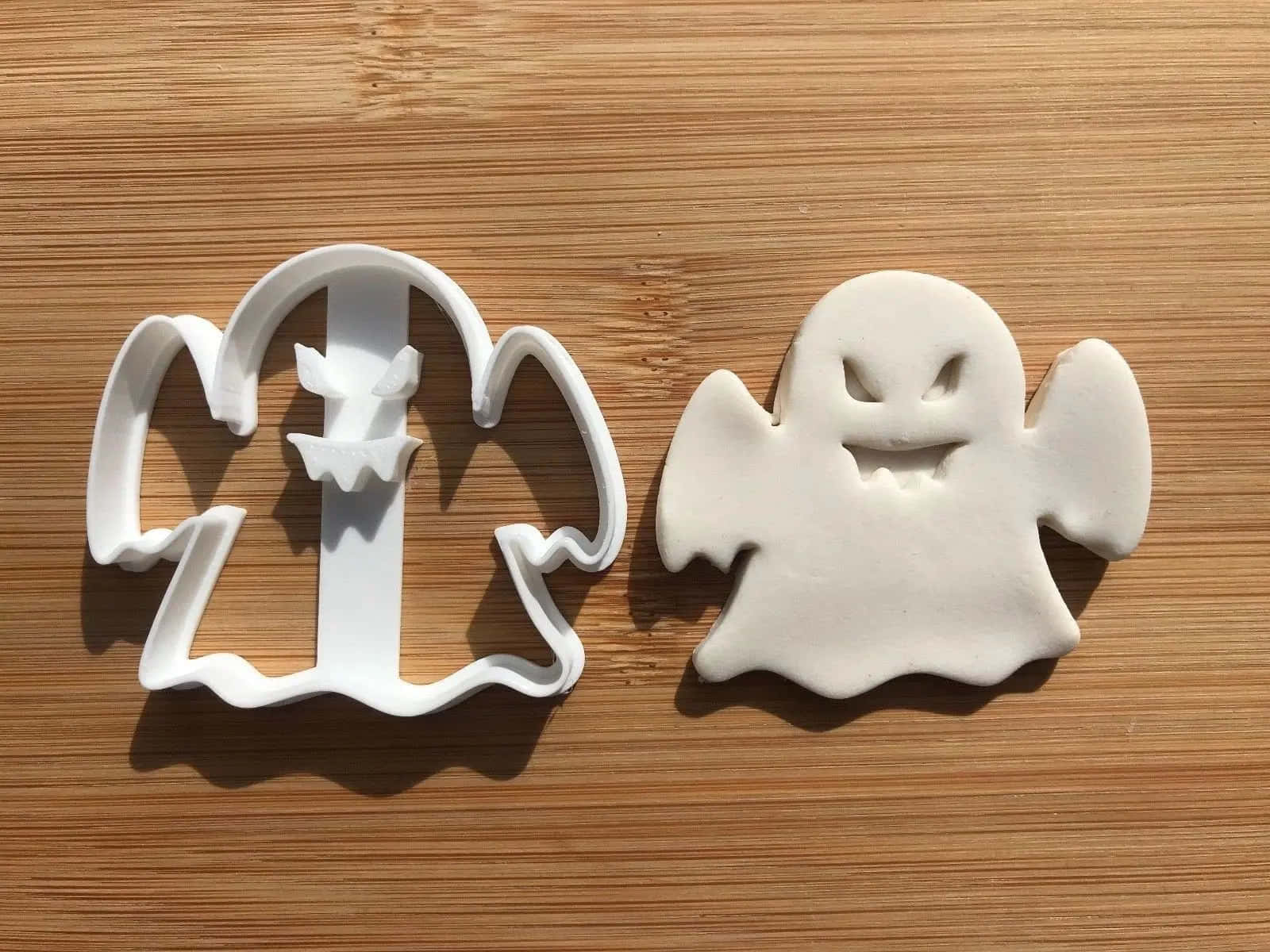 Halloween Cookie Cutters 桌布 壁紙 — 一個白色鬼魂形狀的餅乾模具和一個相應的麵糰切割件放在淺棕色木質表面上。