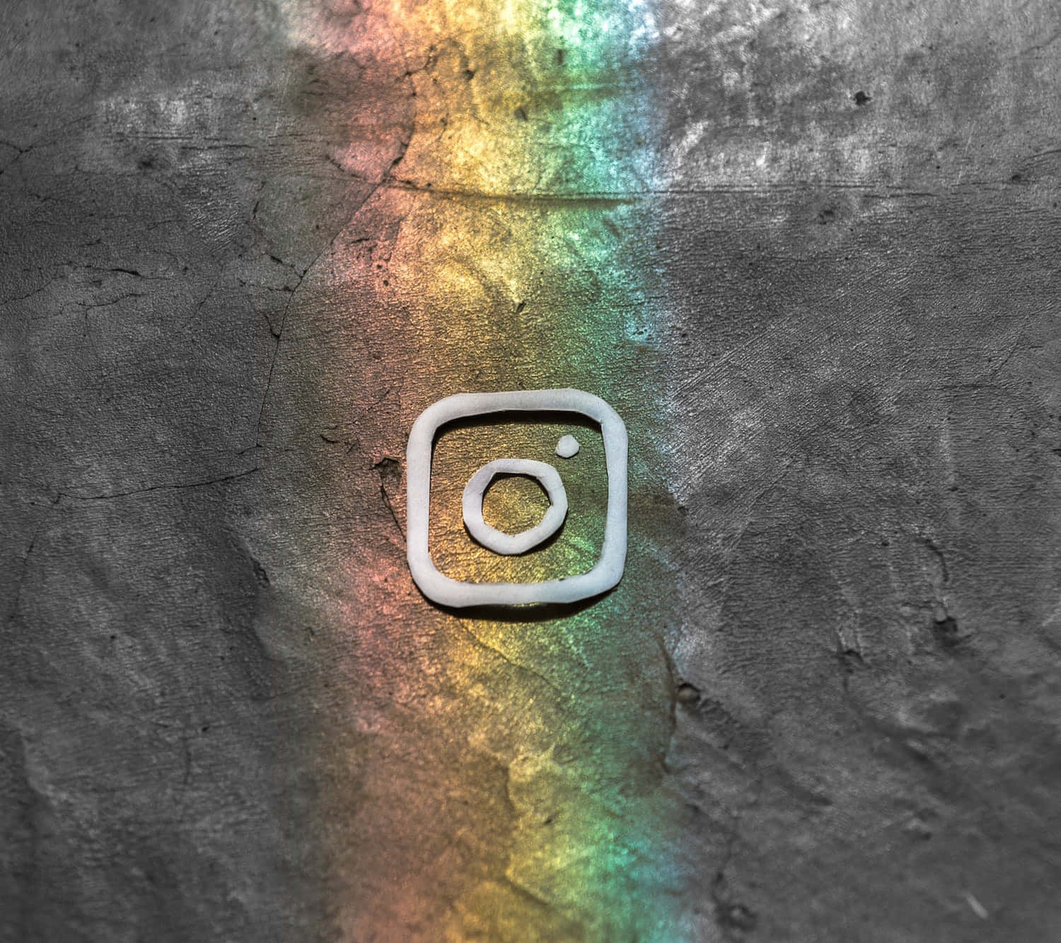 Instagram 桌布 壁紙 — 一個白色黏土Instagram標誌放在裂開的混凝土上，被鮮豔的彩虹光反射照亮。
