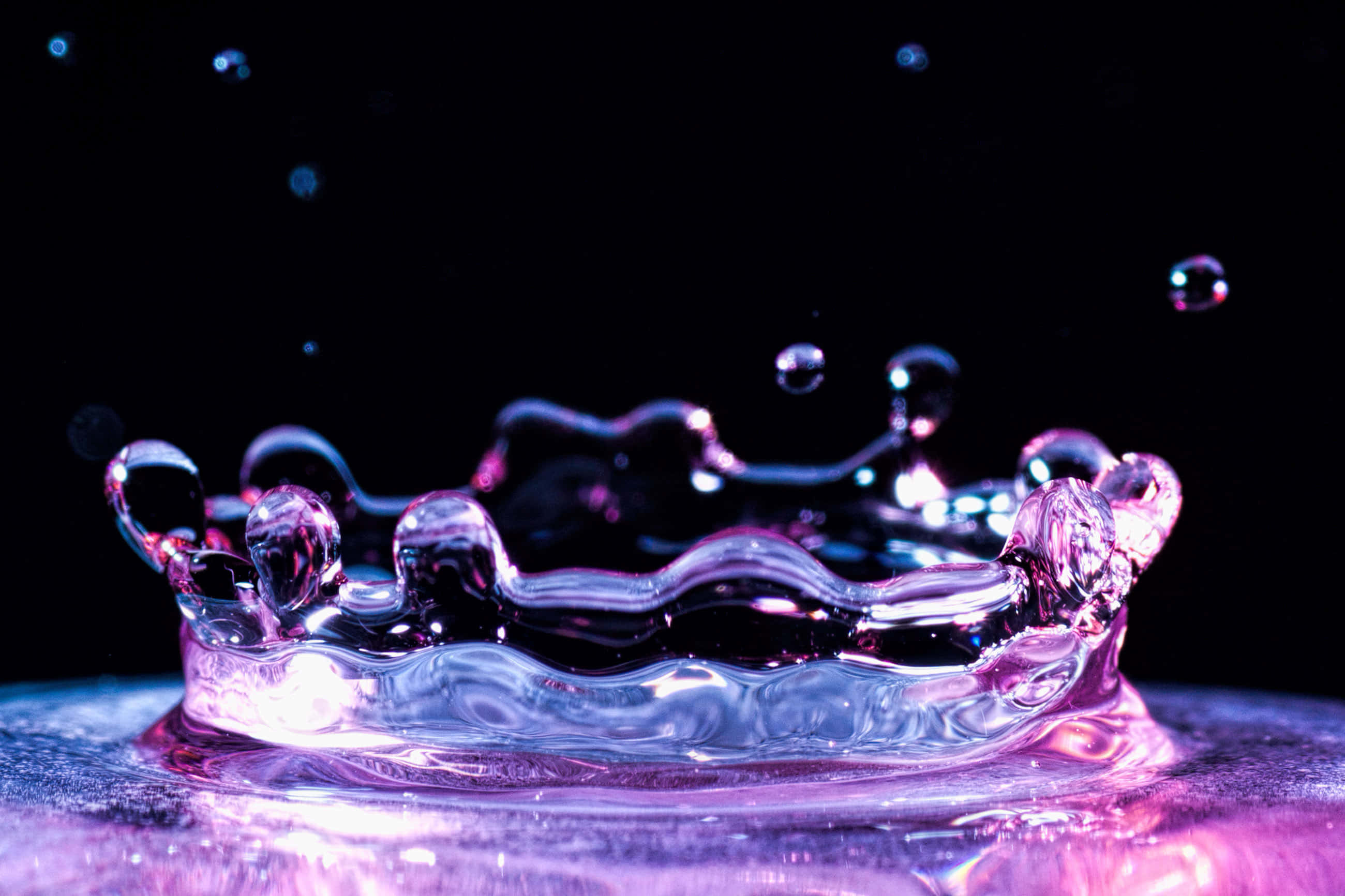 Splash 桌布 壁紙 — 一個皇冠形狀的水花在黑色背景上閃爍著紫色和藍色的光芒。