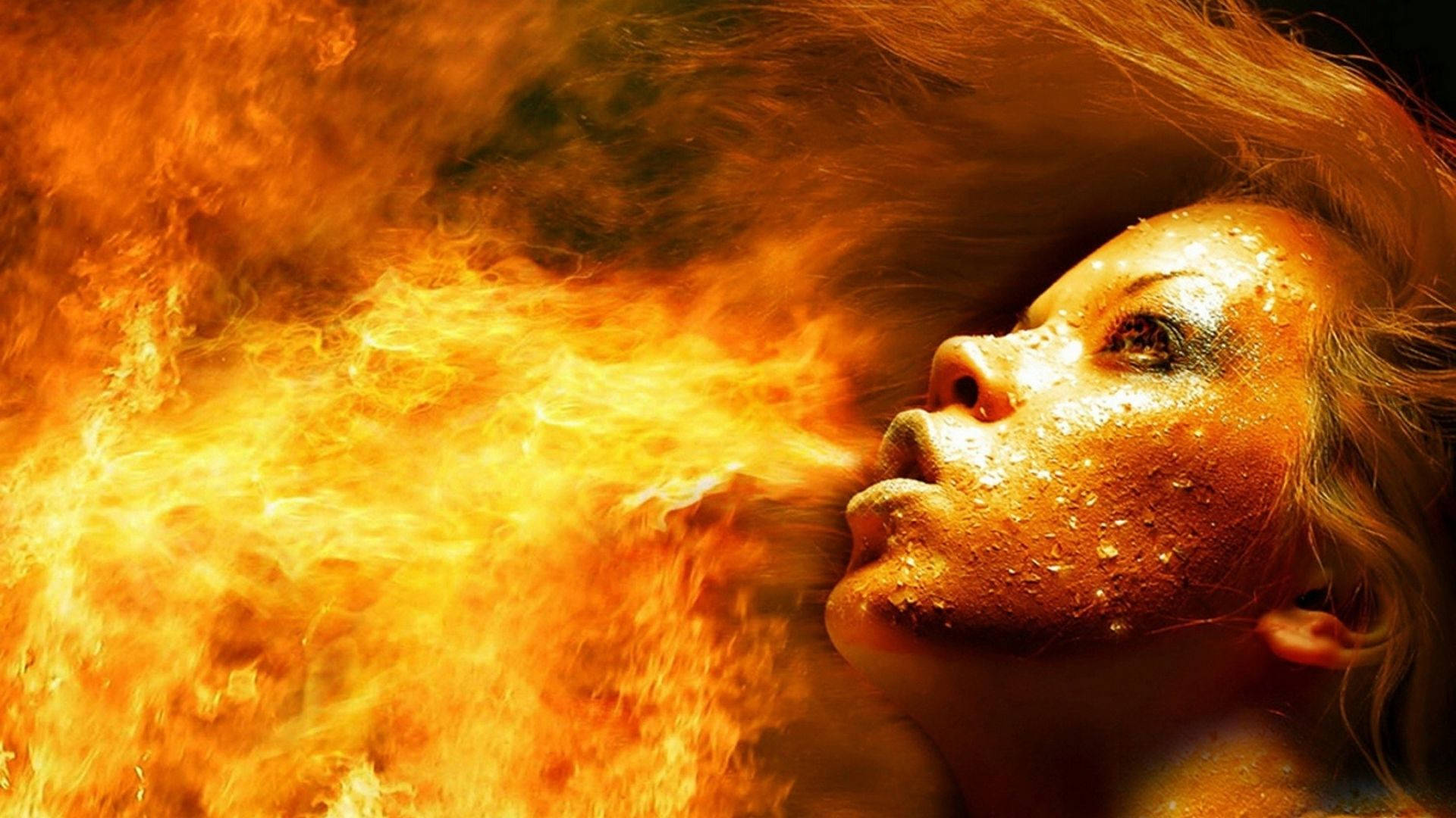 Fire Girl 桌布 壁紙 — 一個皮膚和頭髮濕透的女人，在黑暗的背景下呼出一股咆哮的橙色火焰。