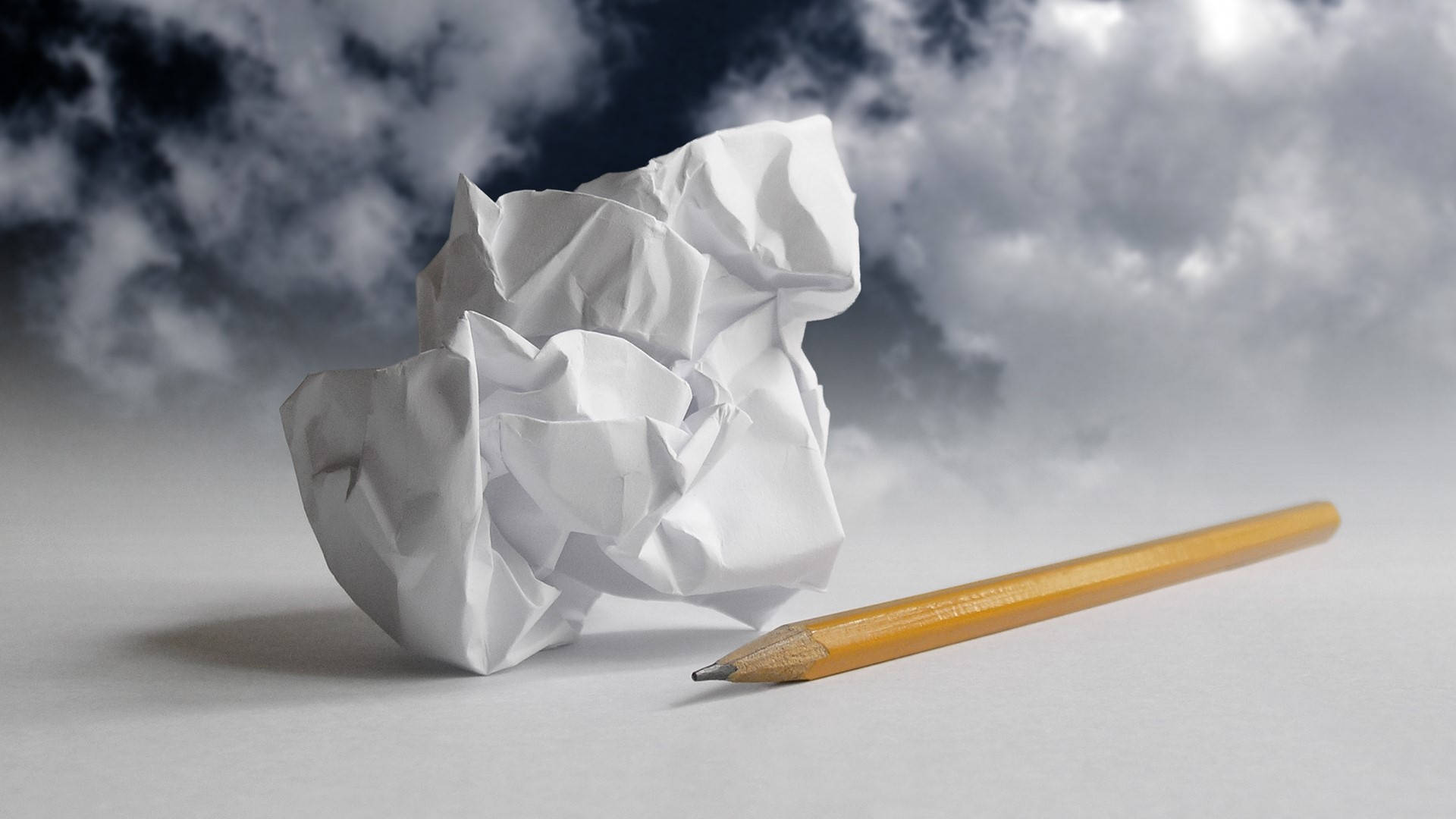 paper 桌布 壁紙 — 一個皺巴巴的白色紙球和黃色鉛筆放在灰色表面上，背景是暴風雨多雲的天空。