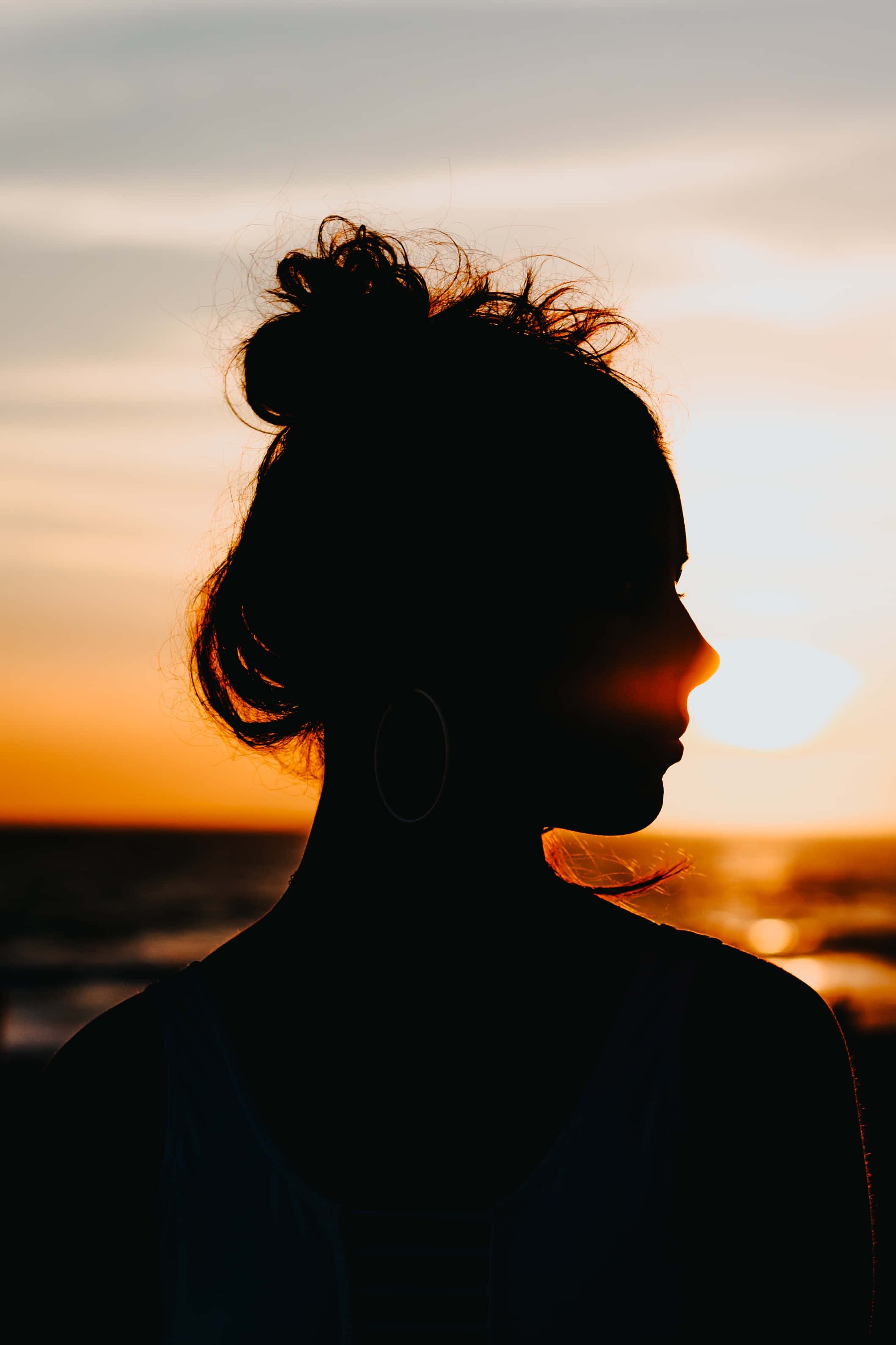 Silhouette 桌布 壁紙 — 一個盤起頭髮的女人剪影，凝視著海洋上閃耀的日落。