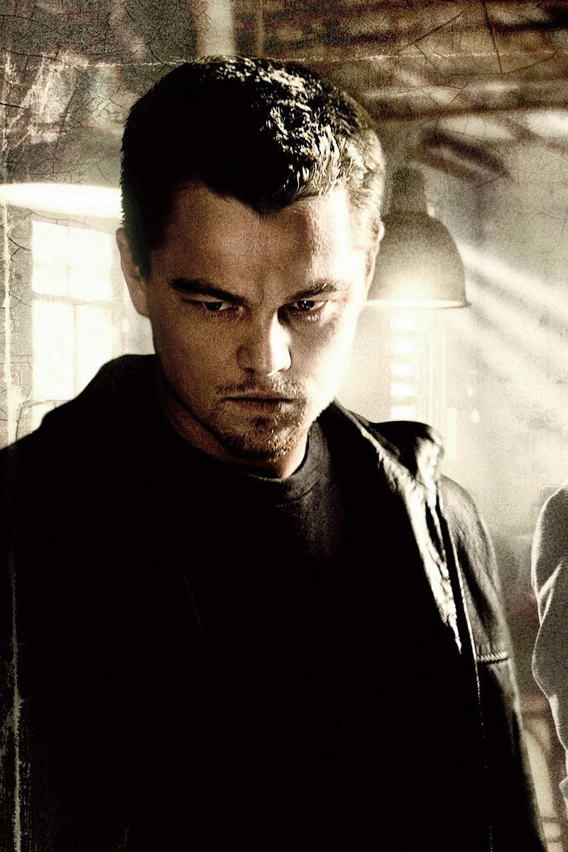 Dicaprio 桌布 壁紙 — 一個眼神銳利、鬍渣未刮的男人，在光線昏暗、帶有戲劇性燈光和紋理牆壁的房間裡凝視前方。