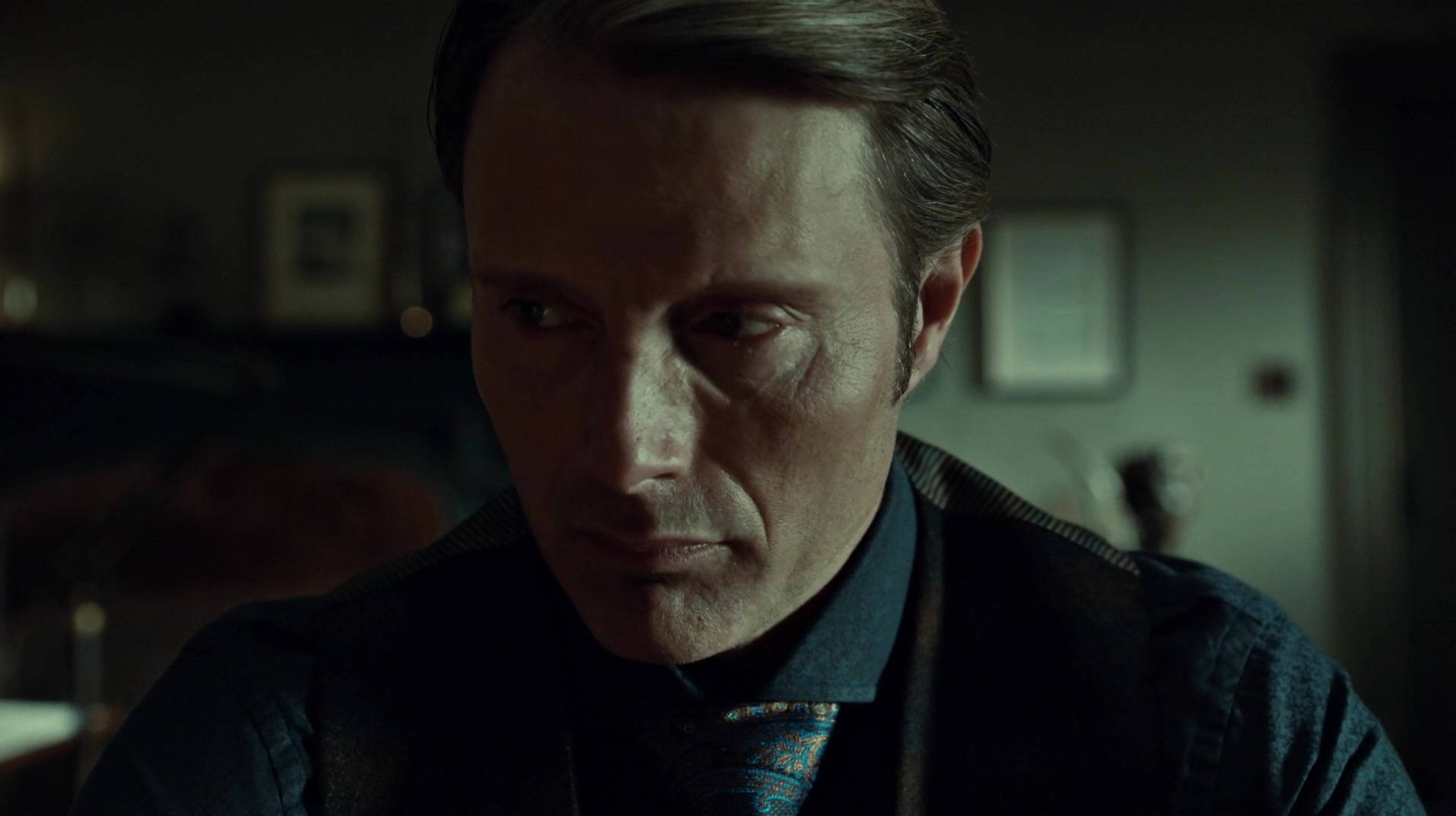 Hannibal 桌布 壁紙 — 一個眼神銳利的男人在昏暗的房間裡向下凝視，帶有柔和的陰影和柔和的色調。
