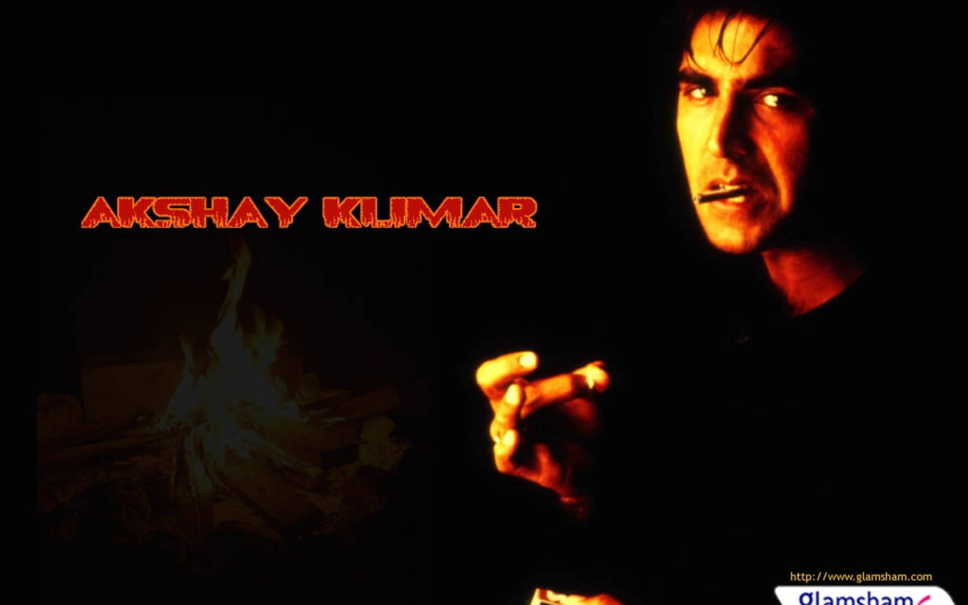Akshay Kumar 桌布 壁紙 — 一個眼神銳利的男人在黑暗背景中手持香煙，背景有火焰文字和發光的營火。