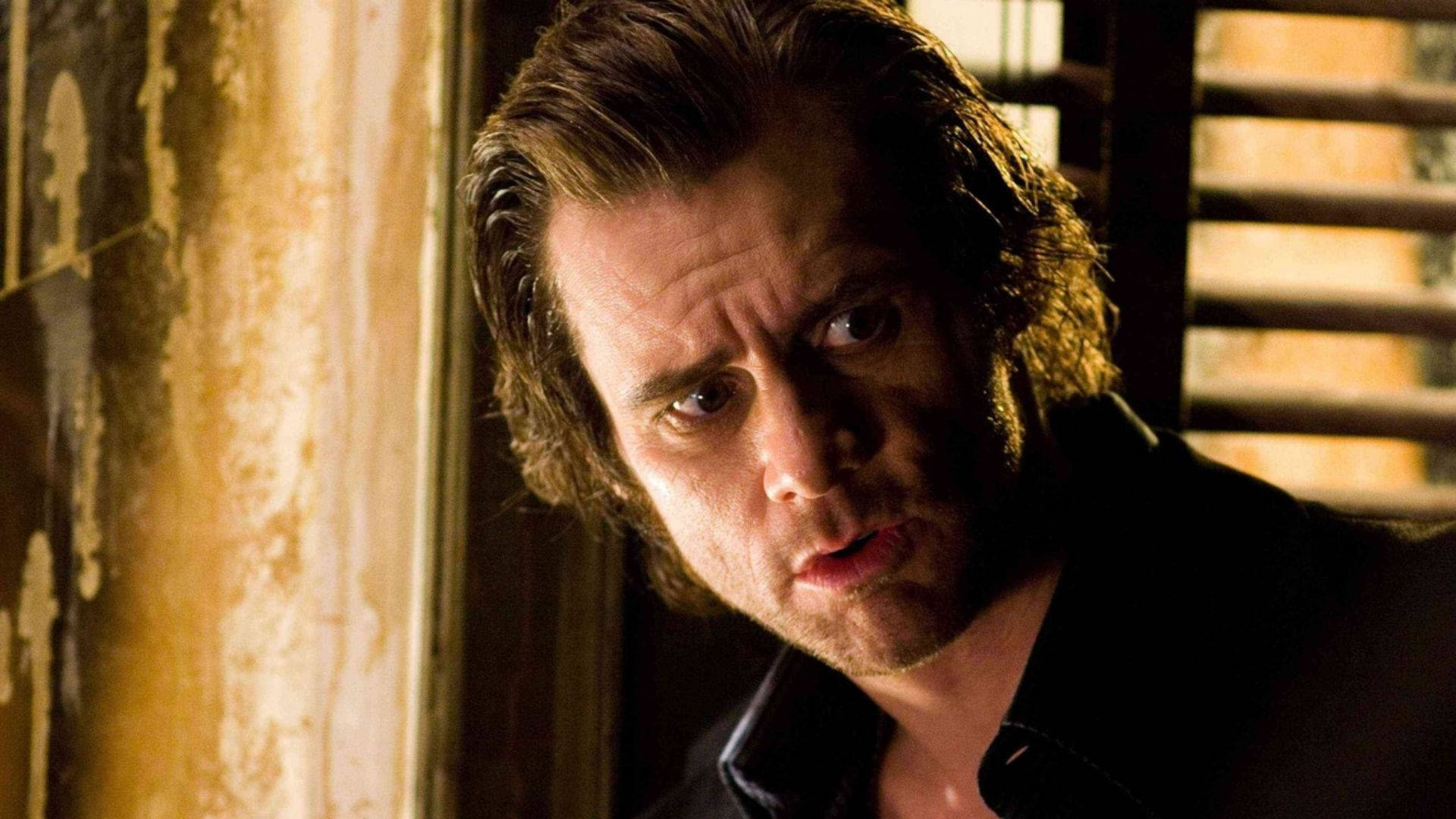 Jim Carrey 桌布 壁紙 — 一個眼神銳利的男人透過百葉窗簾窺視，房間光線昏暗、陳舊，牆壁剝落。