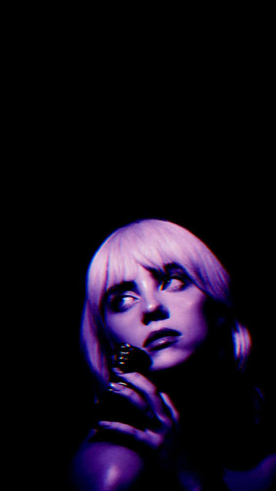 Billie Eilish Purple 桌布 壁紙 — 一個短紫髮的人在黑色背景和戲劇性紫色燈光下向上凝視。