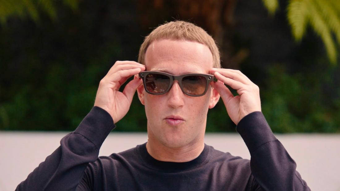 Sunglasses 桌布 壁紙 — 一個短金髮男子在模糊的綠色樹葉背景前，穿著黑色長袖襯衫調整深色太陽眼鏡。
