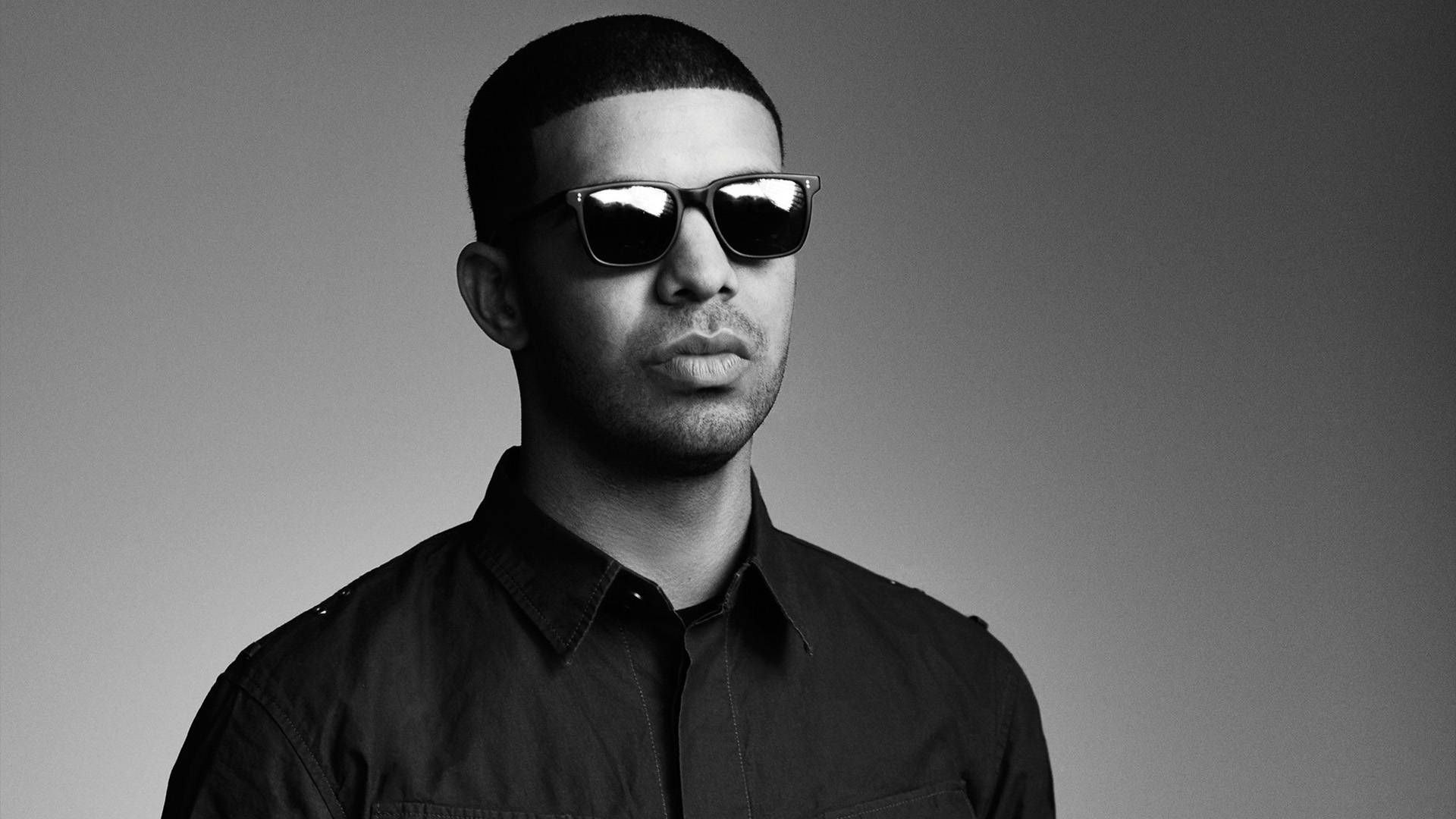 Drake 桌布 壁紙 — 一個短髮男人戴著深色太陽眼鏡和有領襯衫，背景是純灰色，黑白照片。