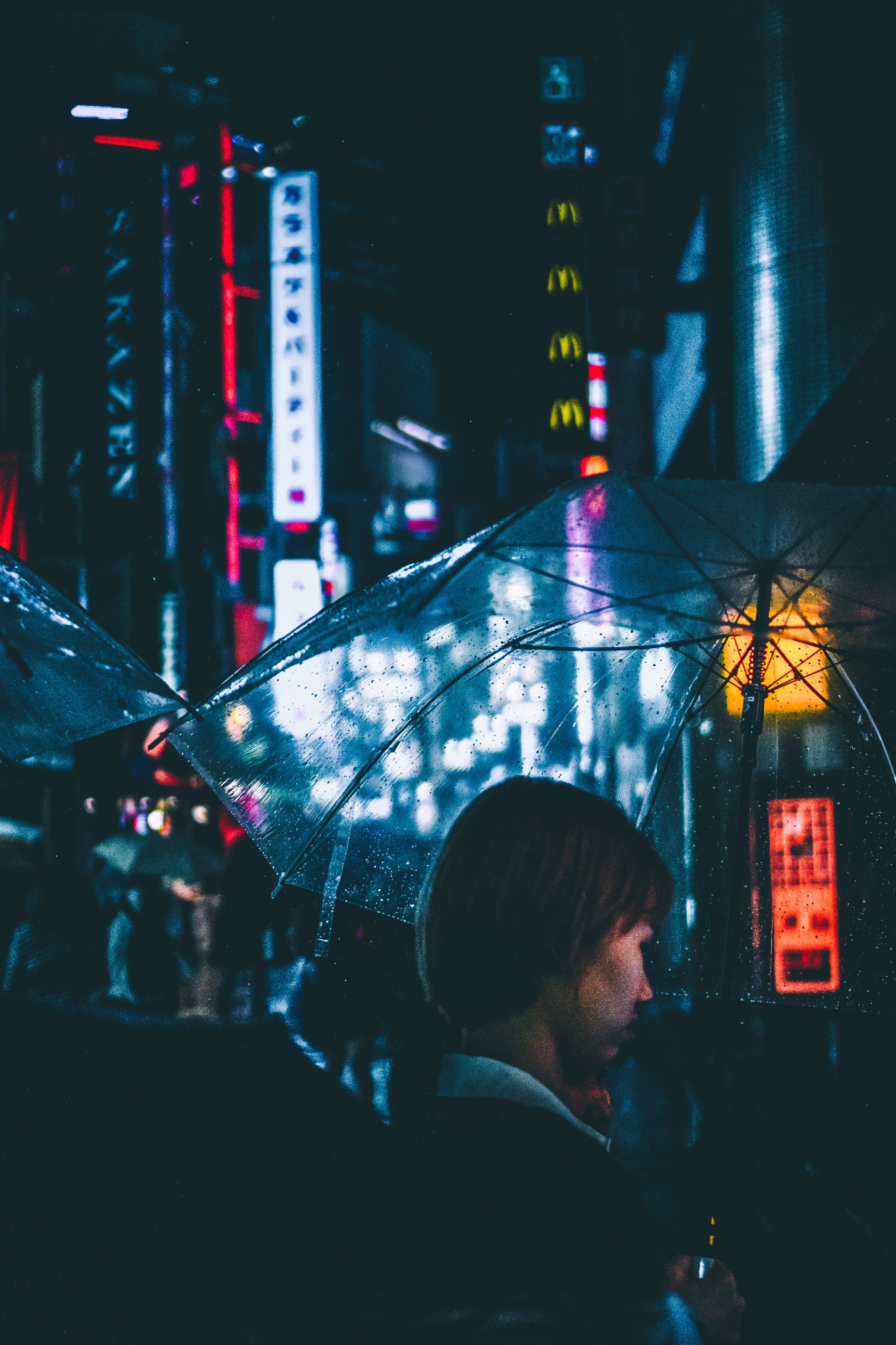 Japanese Girl 桌布 壁紙 — 一個短髮的人拿著一把透明傘，傘上沾滿雨滴，背景是霓虹燈照亮的城市夜景。