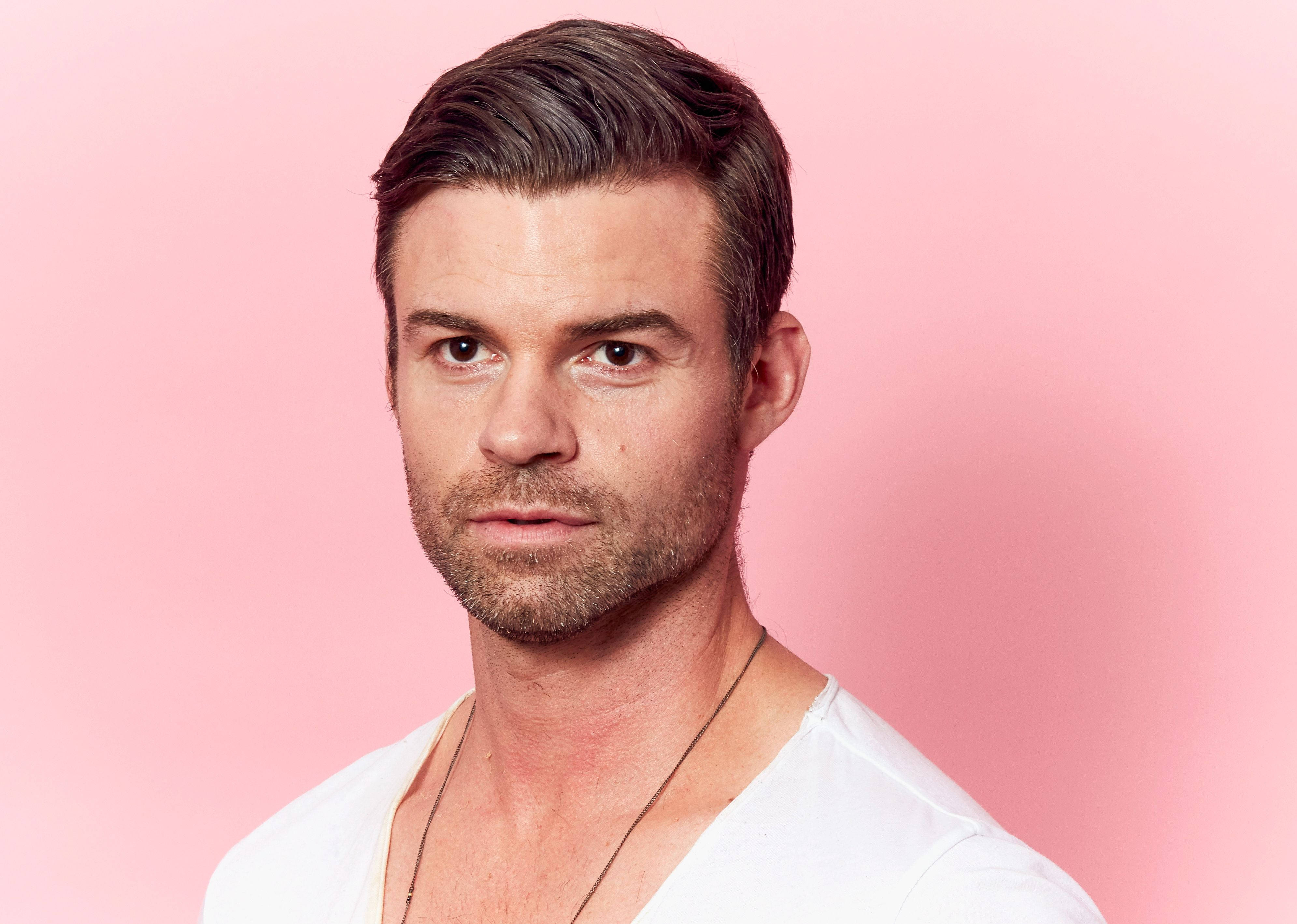 Daniel Gillies 桌布 壁紙 — 一個短黑髮、留鬍渣的男人，在純粉紅色背景前直視鏡頭。