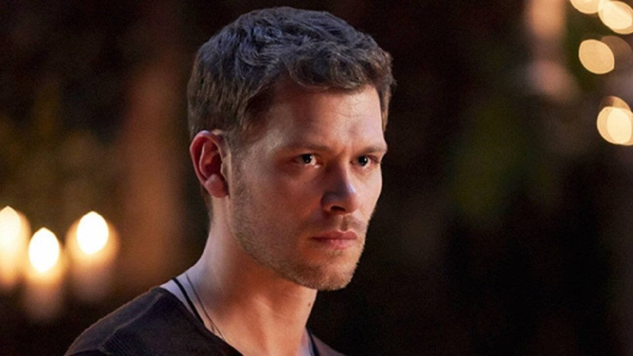 Vampire Diaries 桌布 壁紙 — 一個短黑髮、鬍渣的男人，在柔和模糊的溫暖燈光背景下凝視著。