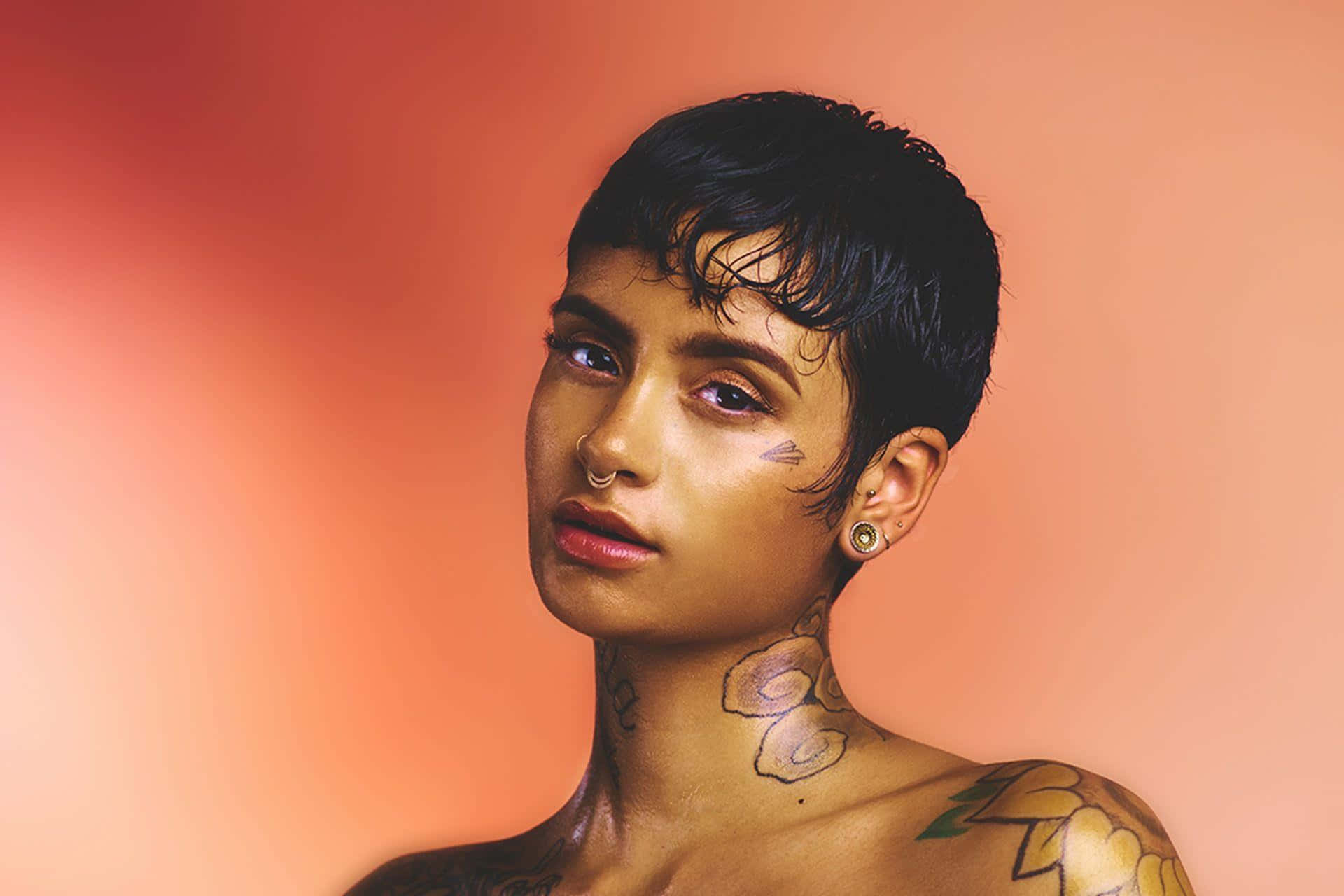 kehlani 桌布 壁紙 — 一個短黑髮及有刺青的人，在溫暖的漸層蜜桃色背景前沉思地凝視。