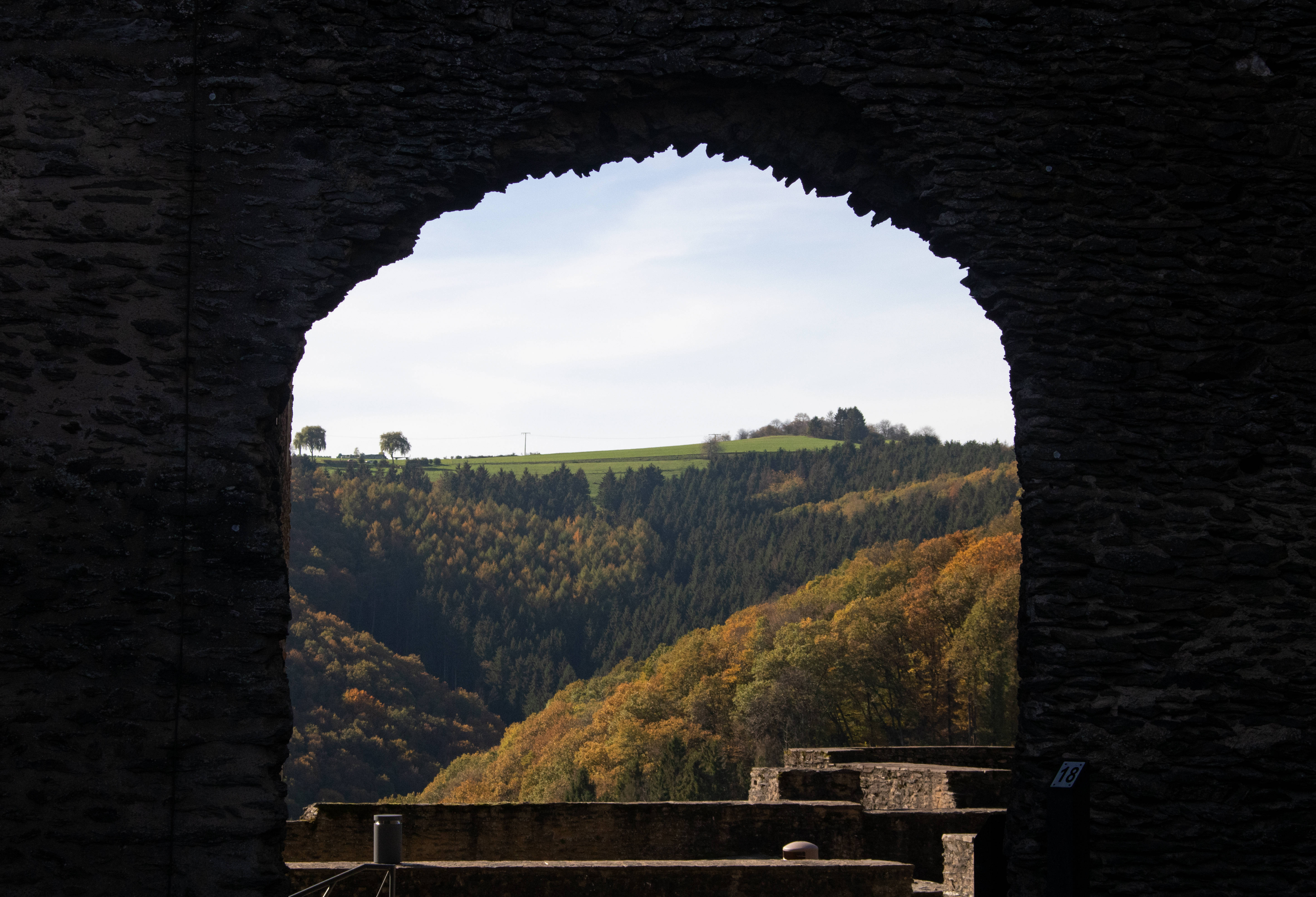 Luxembourg 桌布 壁紙 — 一個石拱門框住了在柔和藍天下綿延起伏的山丘上充滿活力的秋日森林。