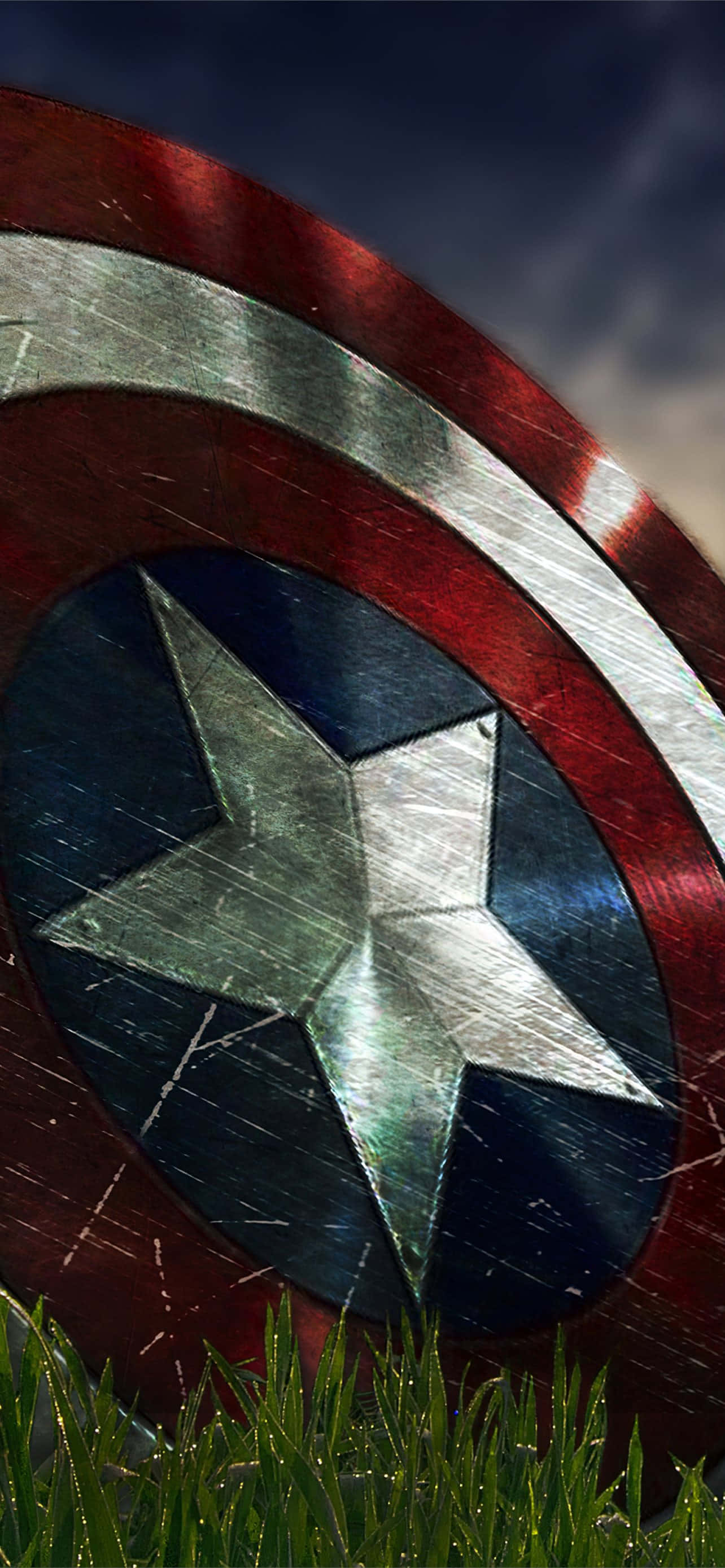Android Captain America 桌布 壁紙 — 一個破損的美國隊長盾牌擱在帶露水的草地上，背景是暴風雨的天空和戲劇性的光線。