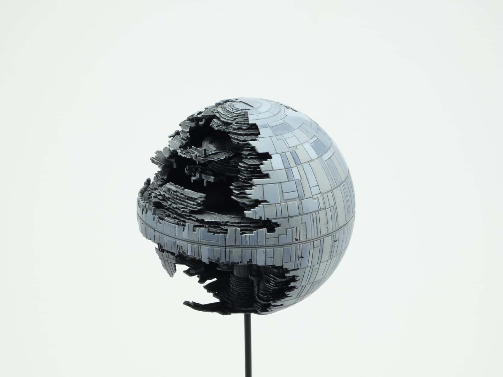 Death Star Ii 桌布 壁紙 — 一個破碎的死星模型，帶有碎裂的金屬板，立在白色背景的底座上。