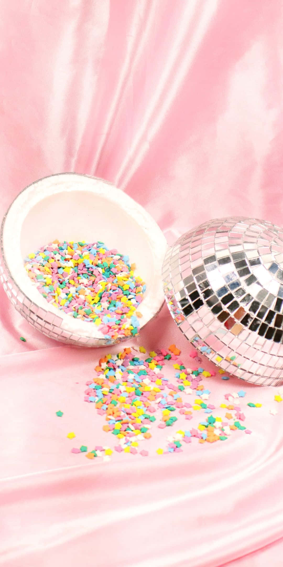 Sprinkles 桌布 壁紙 — 一個破碎的迪斯可球將彩虹糖屑灑在柔軟的粉紅色緞布上。