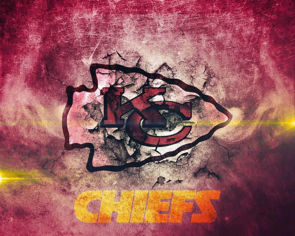 Kc Chiefs 桌布 壁紙 — 一個破舊的堪薩斯城酋長隊標誌從裂開的混凝土中浮現，帶有火橙色和栗色的煙霧效果。