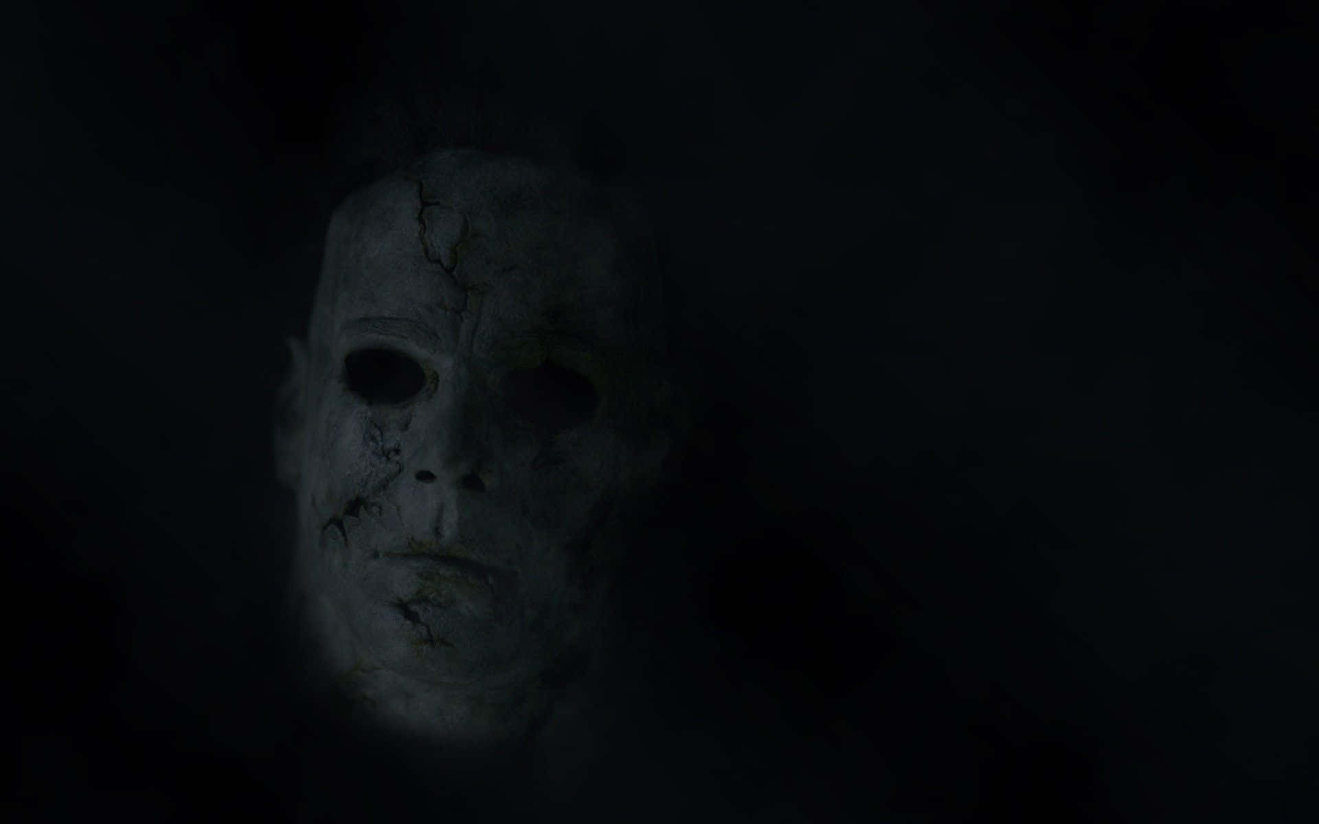 Cool Scary 桌布 壁紙 — 一個破裂的白色面具在完全黑暗中微弱發光，露出空洞的眼睛和威脅的表情。