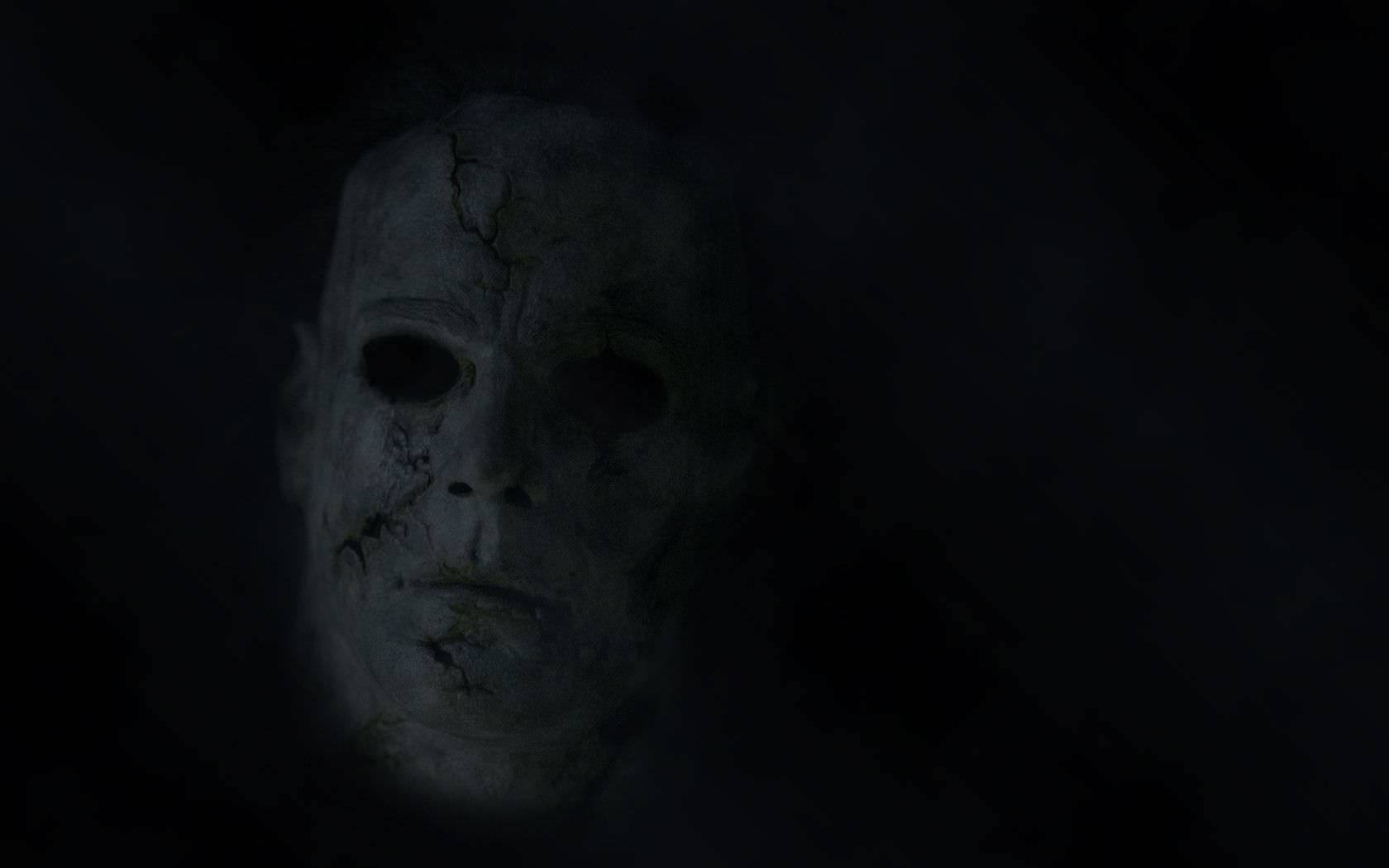 Scared 桌布 壁紙 — 一個破裂的白色面具在完全黑暗中發出微弱的光芒，喚起恐怖和懸念。