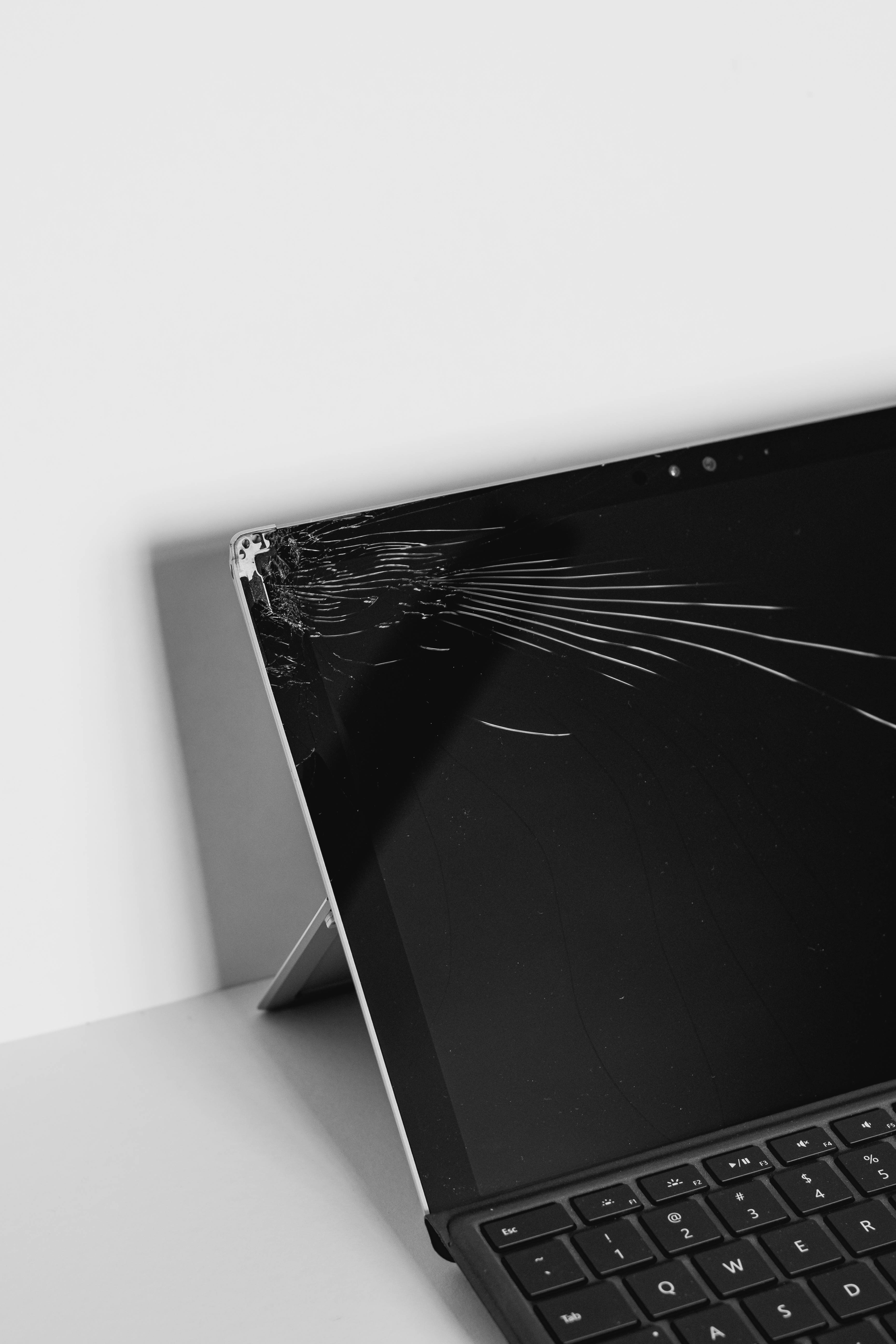 broken monitor 桌布 壁紙 — 一個破裂的筆記型電腦螢幕靠在白色牆壁上，處於極簡主義的黑白環境中。