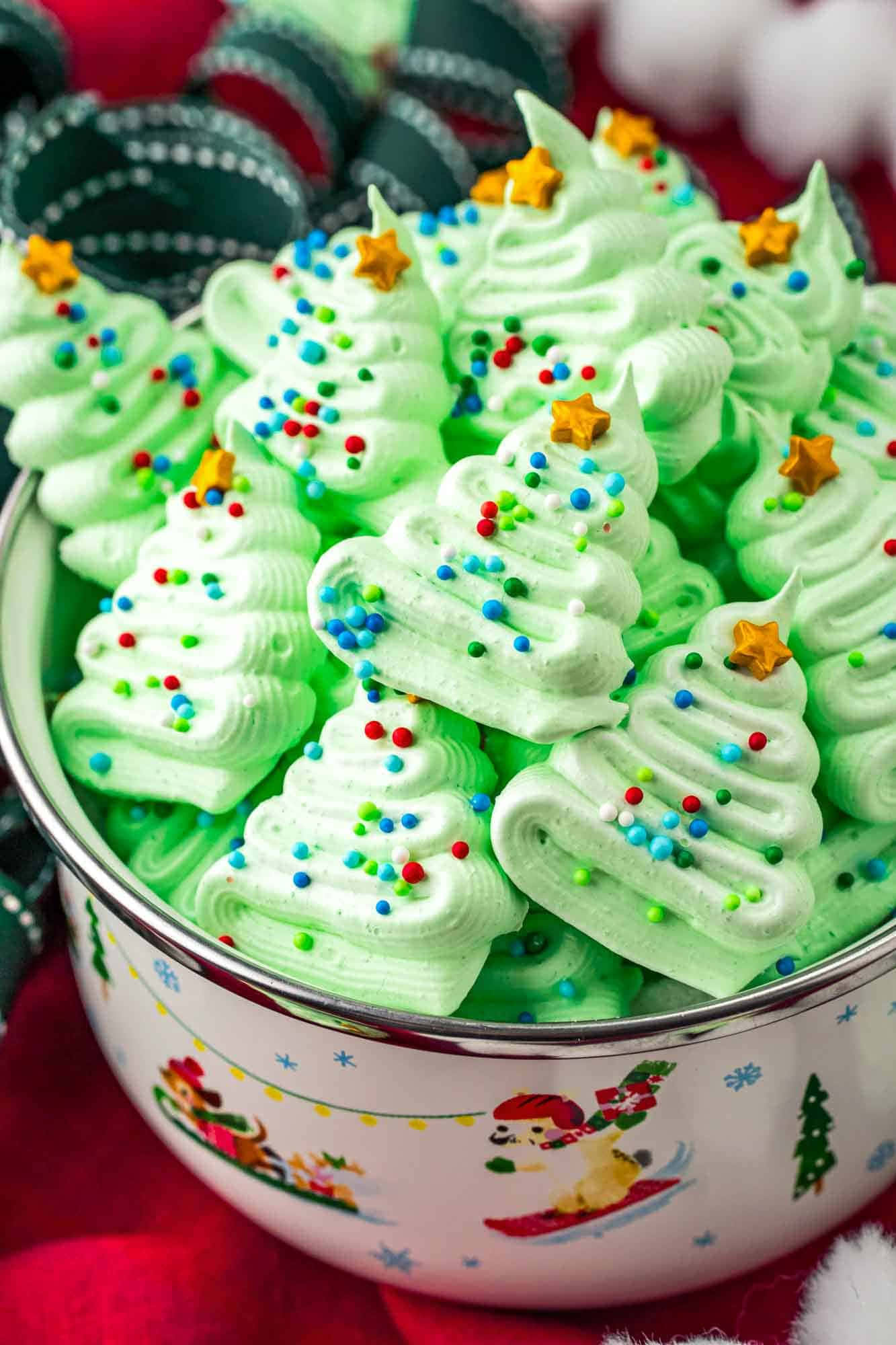 Meringue 桌布 壁紙 — 一個碗裡裝滿了聖誕樹形狀的節日綠色蛋白霜餅乾，上面撒滿了彩色糖粒和金色星星。