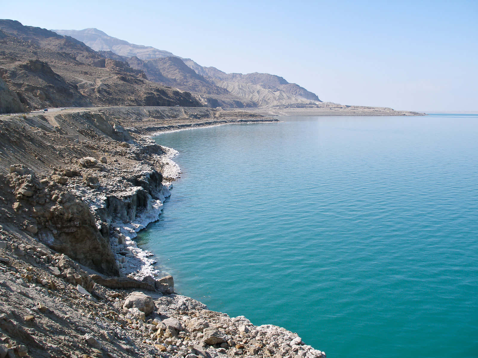 Jordan 桌布 壁紙 — 一個碧綠色的湖泊擁抱著崎嶇乾旱的海岸線，天空湛藍清澈，遠山連綿。