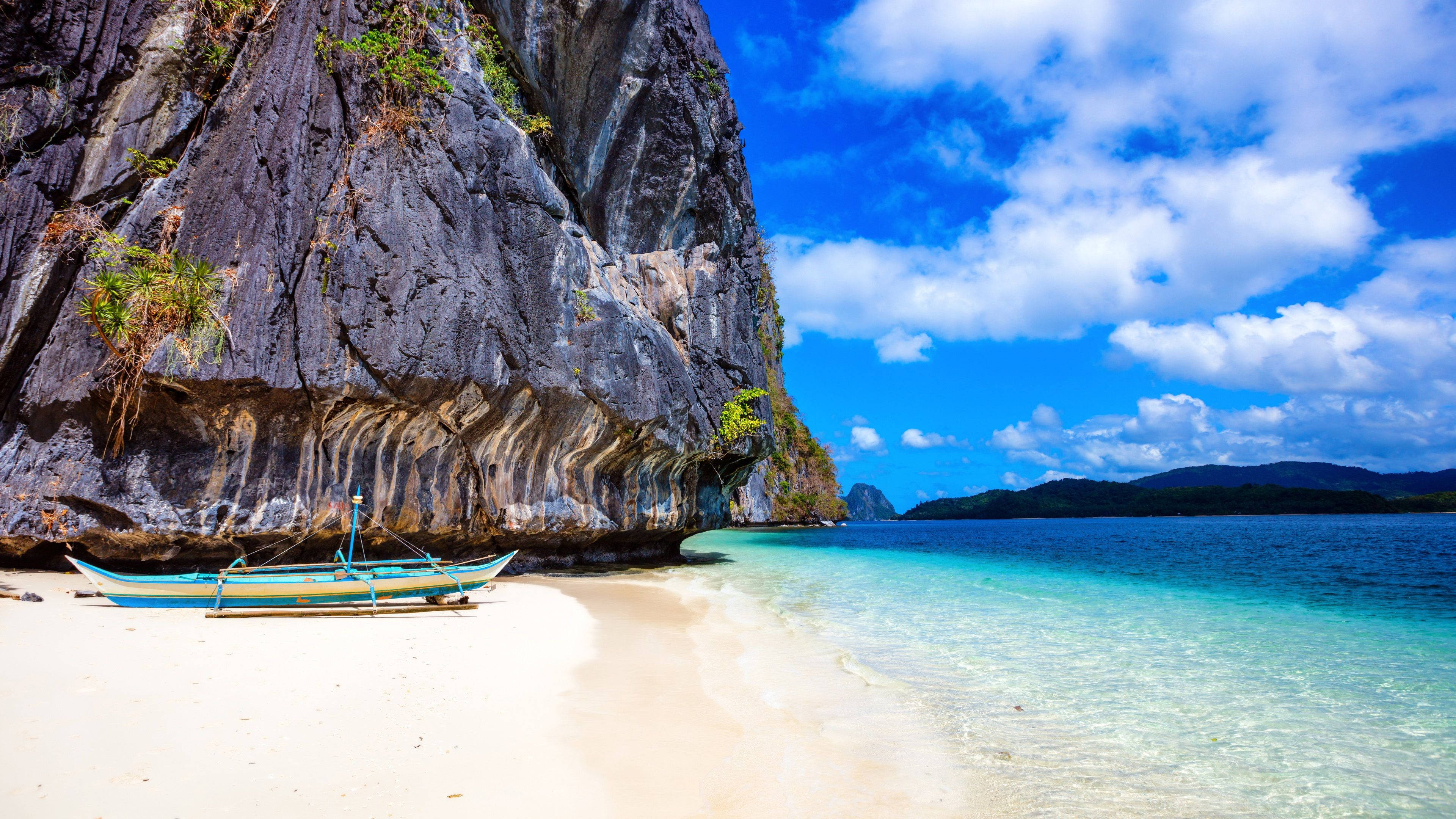 Philippines 桌布 壁紙 — 一個碧綠色的潟湖拍打著白色沙灘，旁邊是高聳的灰色懸崖，上方是晴朗的藍天和蓬鬆的白雲。