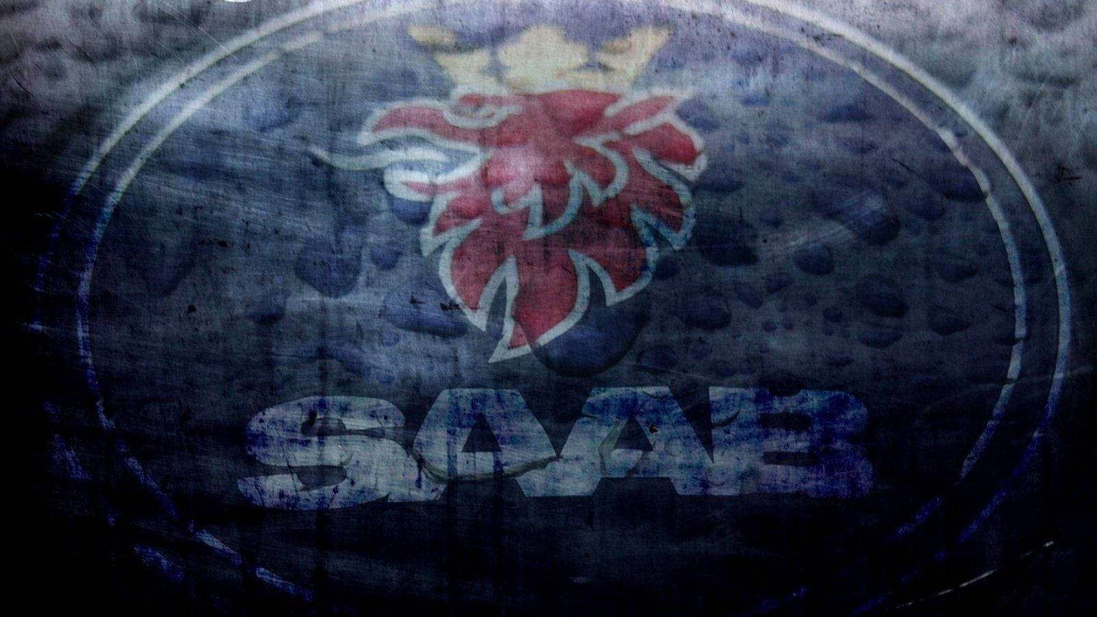 Saab 桌布 壁紙 — 一個磨損的SAAB標誌，帶有紅色皇冠獅子徽章，位於深色紋理表面上。