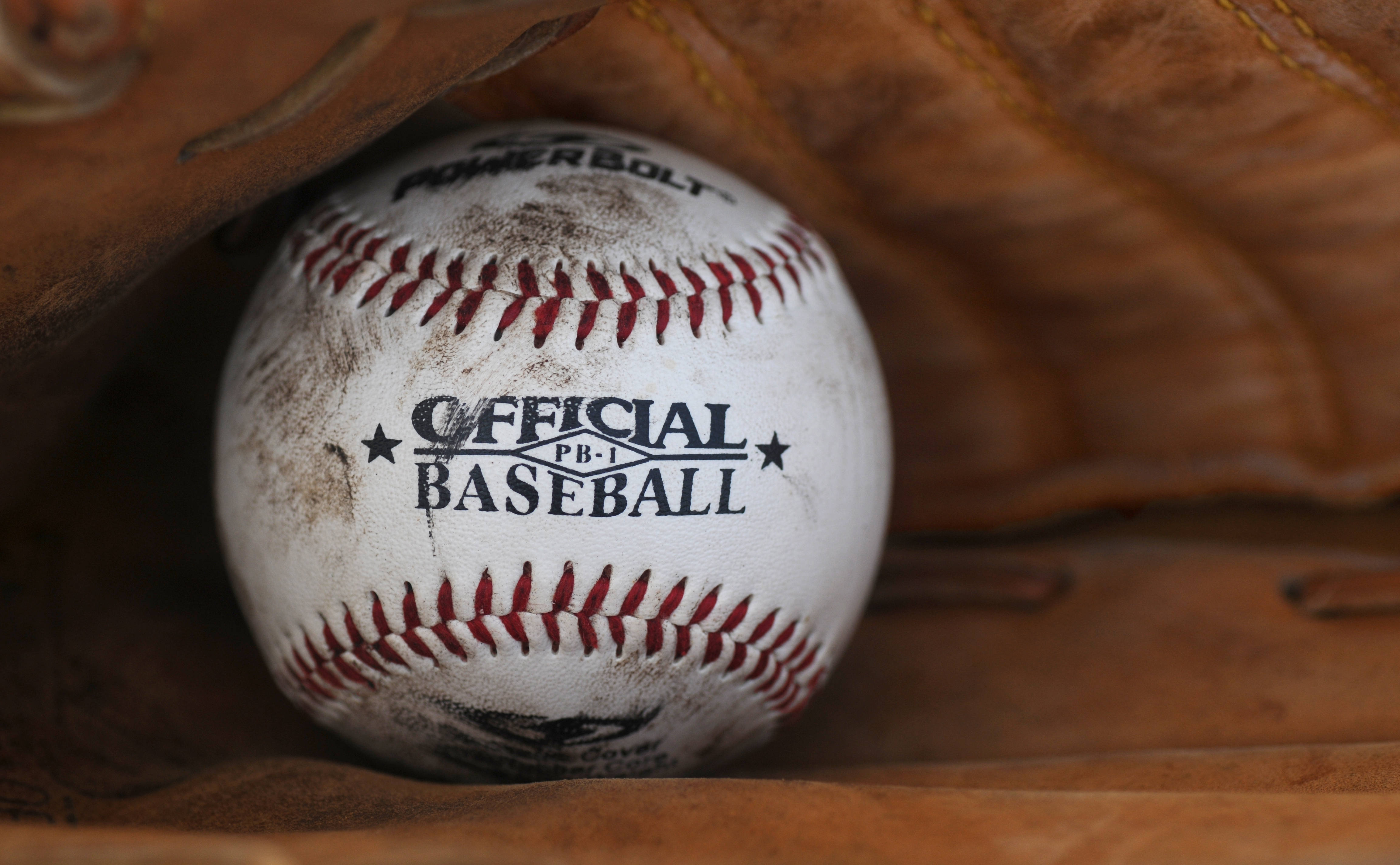 MLB 桌布 壁紙 — 一個磨損的官方棒球近距離特寫，放在棕色皮手套中，顯示污垢和紅色縫線。