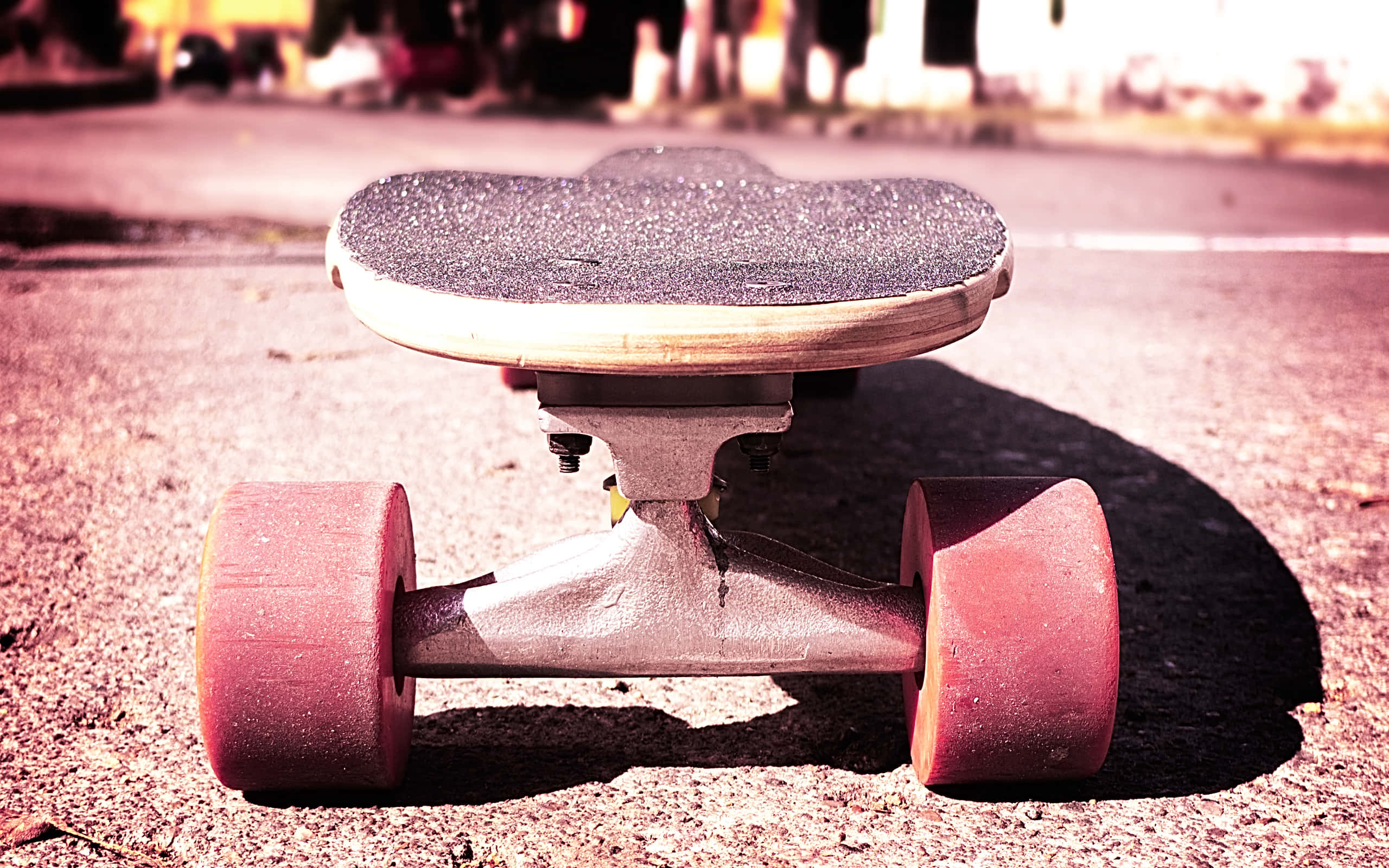 Retro Skateboard 桌布 壁紙 — 一個磨損的滑板，帶有粉紅色輪子，在溫暖的陽光下擱在瀝青上的特寫。