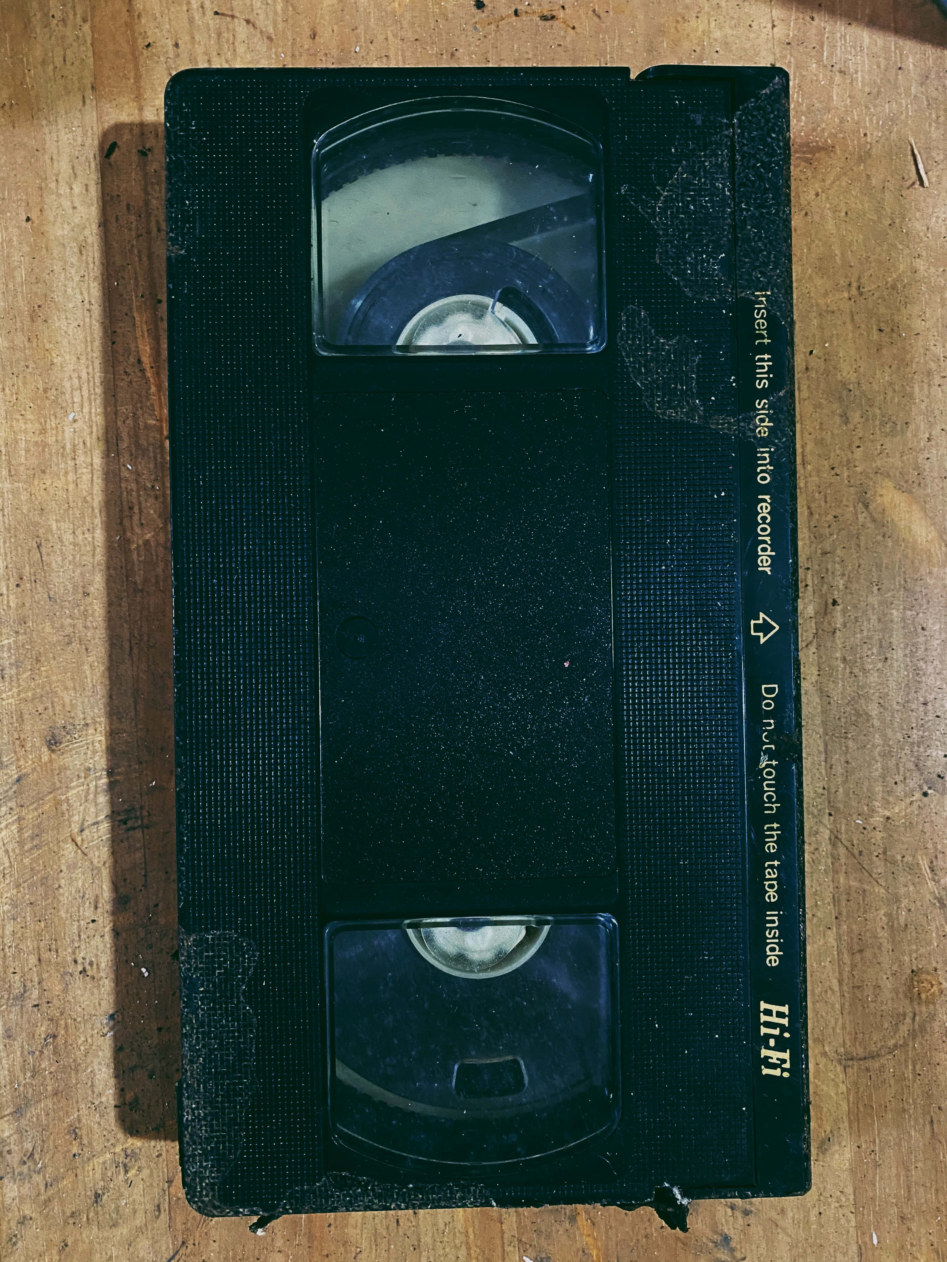 vhs 桌布 壁紙 — 一個磨損的黑色VHS錄影帶放在一塊風化的木質表面上，顯示出歲月和使用痕跡。