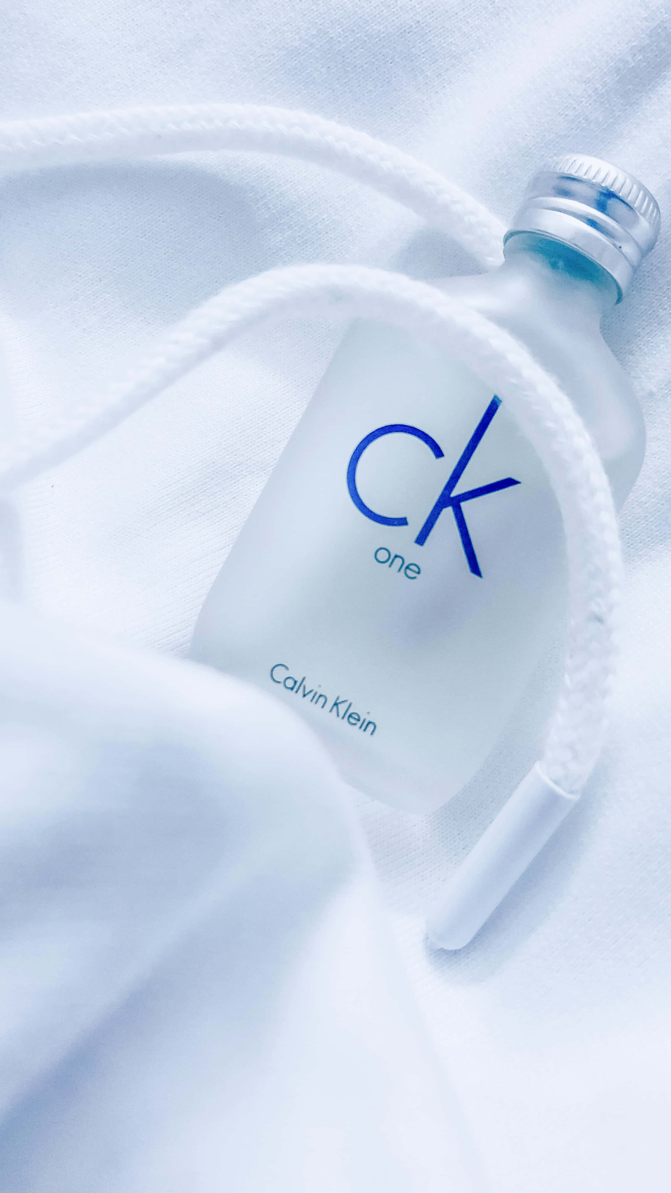 卡文克萊 桌布 壁紙 — 一個磨砂玻璃 Calvin Klein CK One 香水瓶放在柔軟的白色布料上，白色繩索纏繞著。
