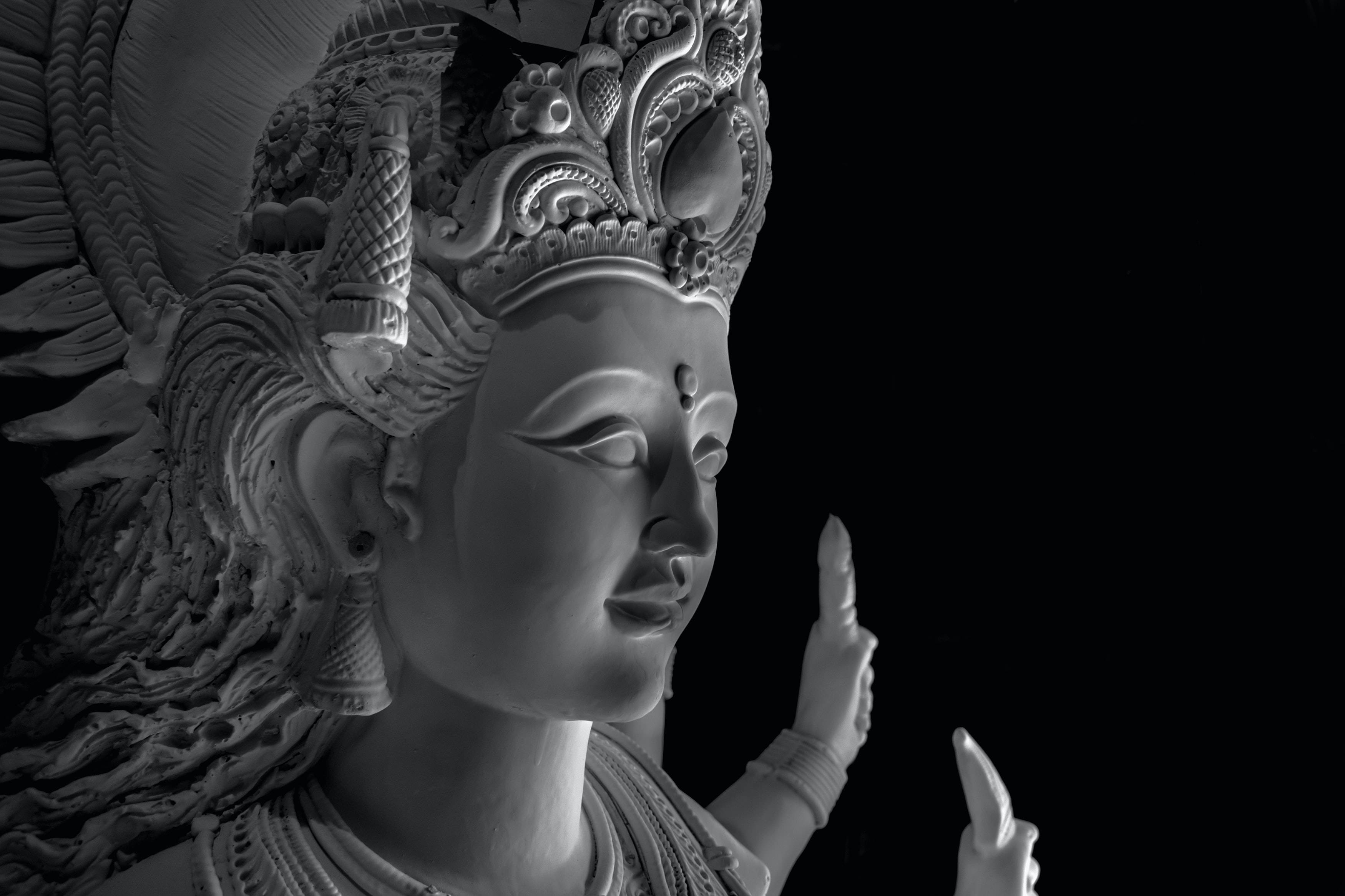 Mata Rani 桌布 壁紙 — 一個神聖人物的寧靜單色雕塑，帶有精緻的頭飾和飄逸的頭髮，背景是純黑色。