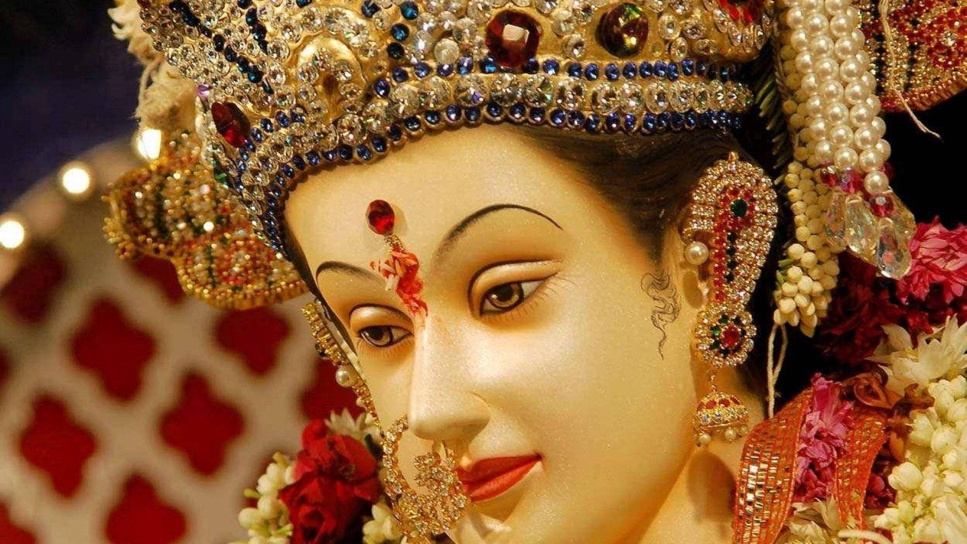 durga mata HD 桌布 壁紙 — 一個神聖偶像的特寫，飾有精緻的金色珠寶、紅色寶石和花環，在溫暖的燈光下閃閃發光。