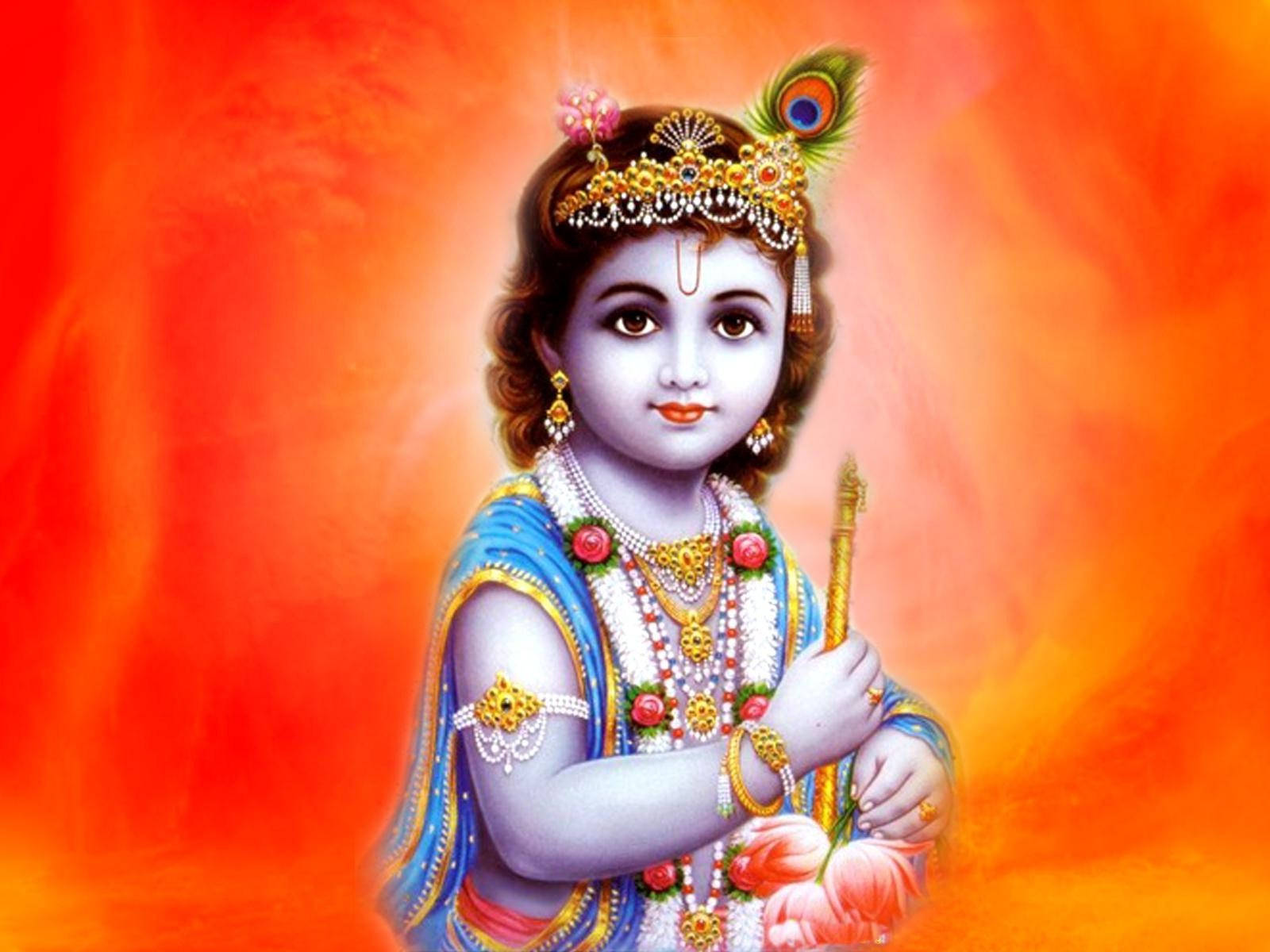 Indian 桌布 壁紙 — 一個神聖的孩子，佩戴著金色珠寶和藍色衣服，在明亮的橙色背景前拿著一支笛子。