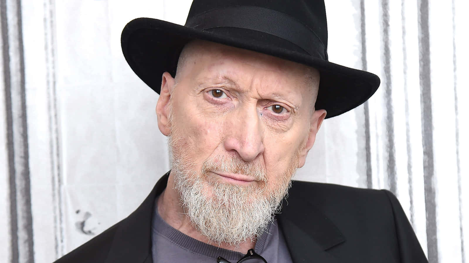 Frank Miller 桌布 壁紙 — 一個禿頭、留白鬍鬚的男人，戴黑色紳士帽、穿西裝，在條紋背景前的特寫肖像。