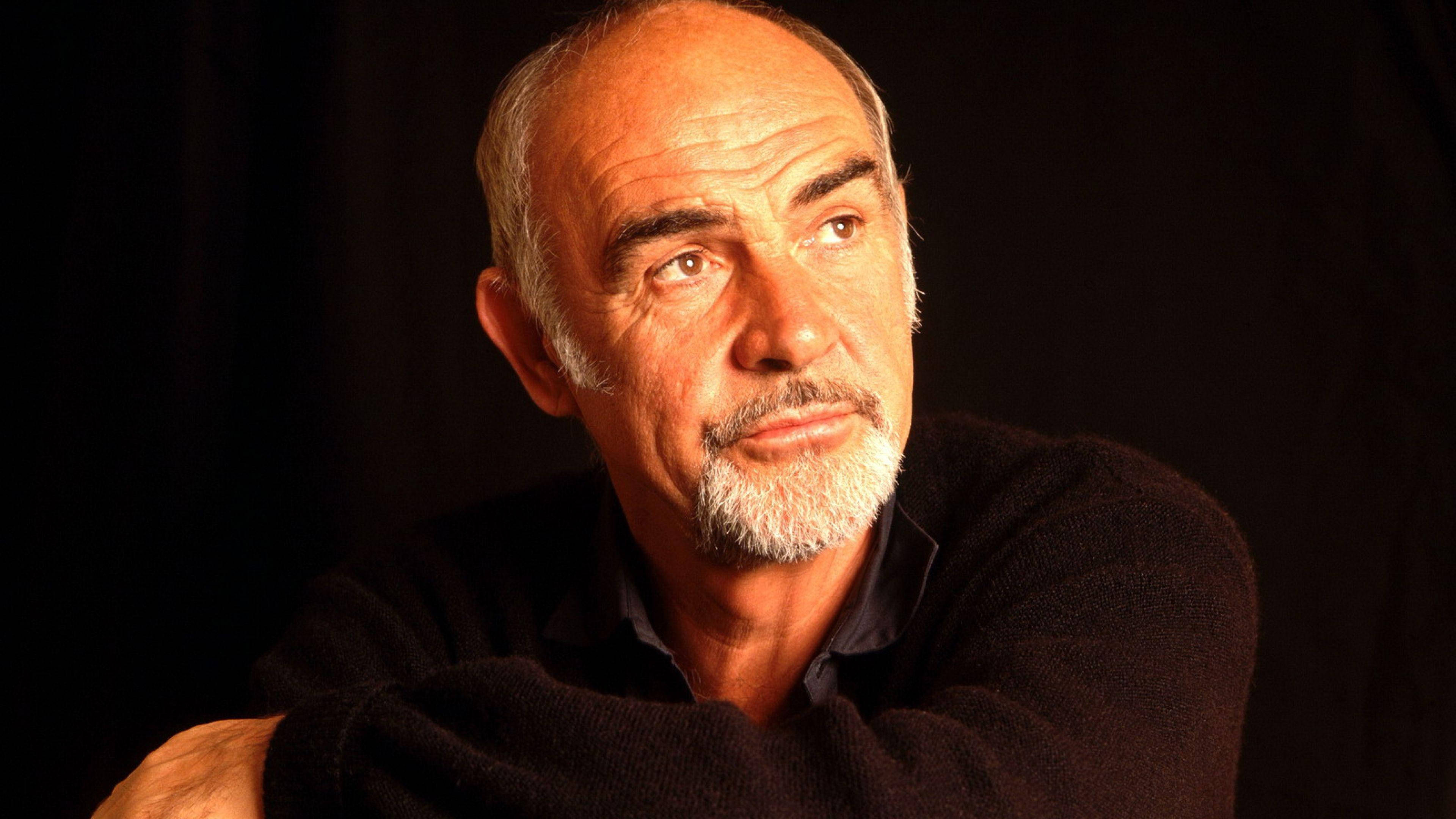 Sean Connery 桌布 壁紙 — 一個禿頭、留著白鬍子的男人穿著深色毛衣，在黑色背景下的特寫肖像。