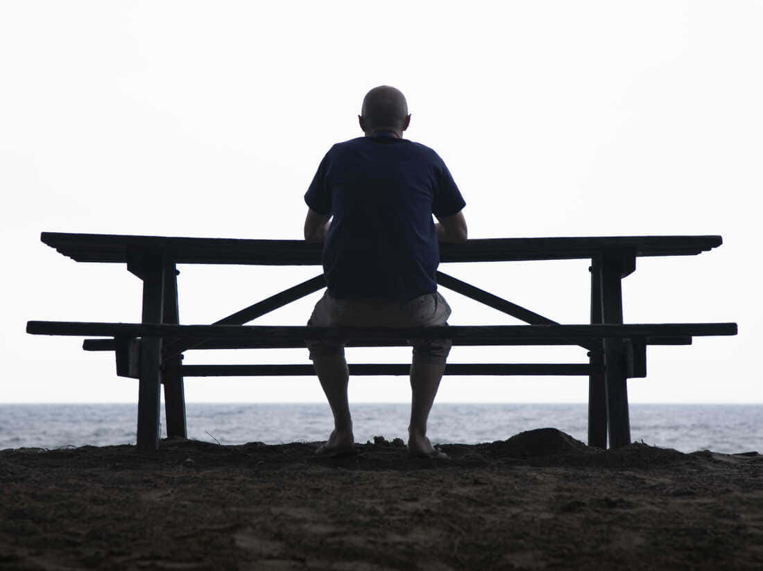 Lonely 桌布 壁紙 — 一個禿頭男人獨自坐在野餐桌旁，在黃昏時俯瞰海洋，在蒼白的天空下形成剪影。