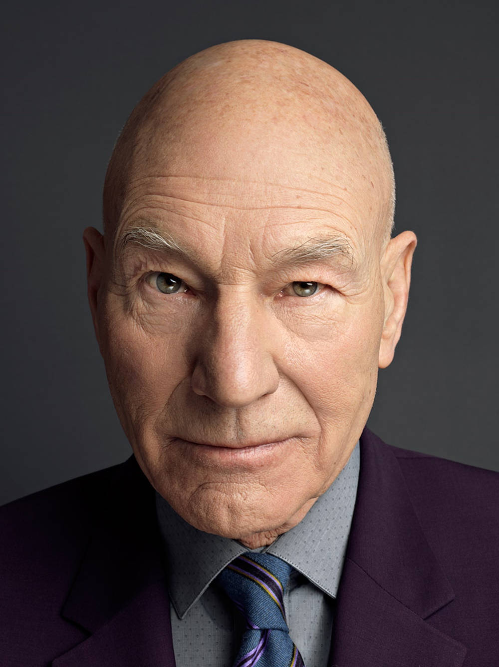 Celebrity 桌布 壁紙 — 一個禿頭老年男子穿著紫色西裝和條紋領帶，在深灰色背景前的特寫肖像。