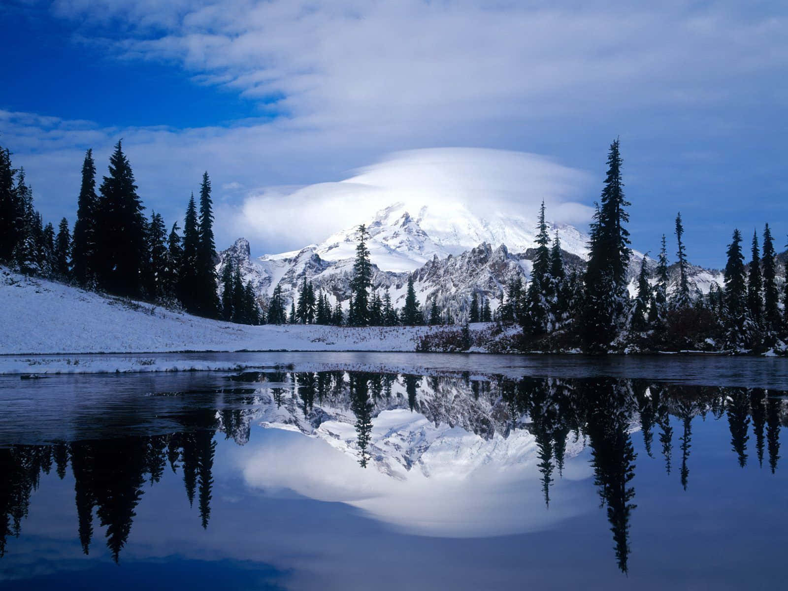 Snowy Mountain 桌布 壁紙 — 一個積雪的山峰，頂上有一片透鏡狀雲，漂浮在平靜的湖面上，湖面倒映著藍天下的景色。