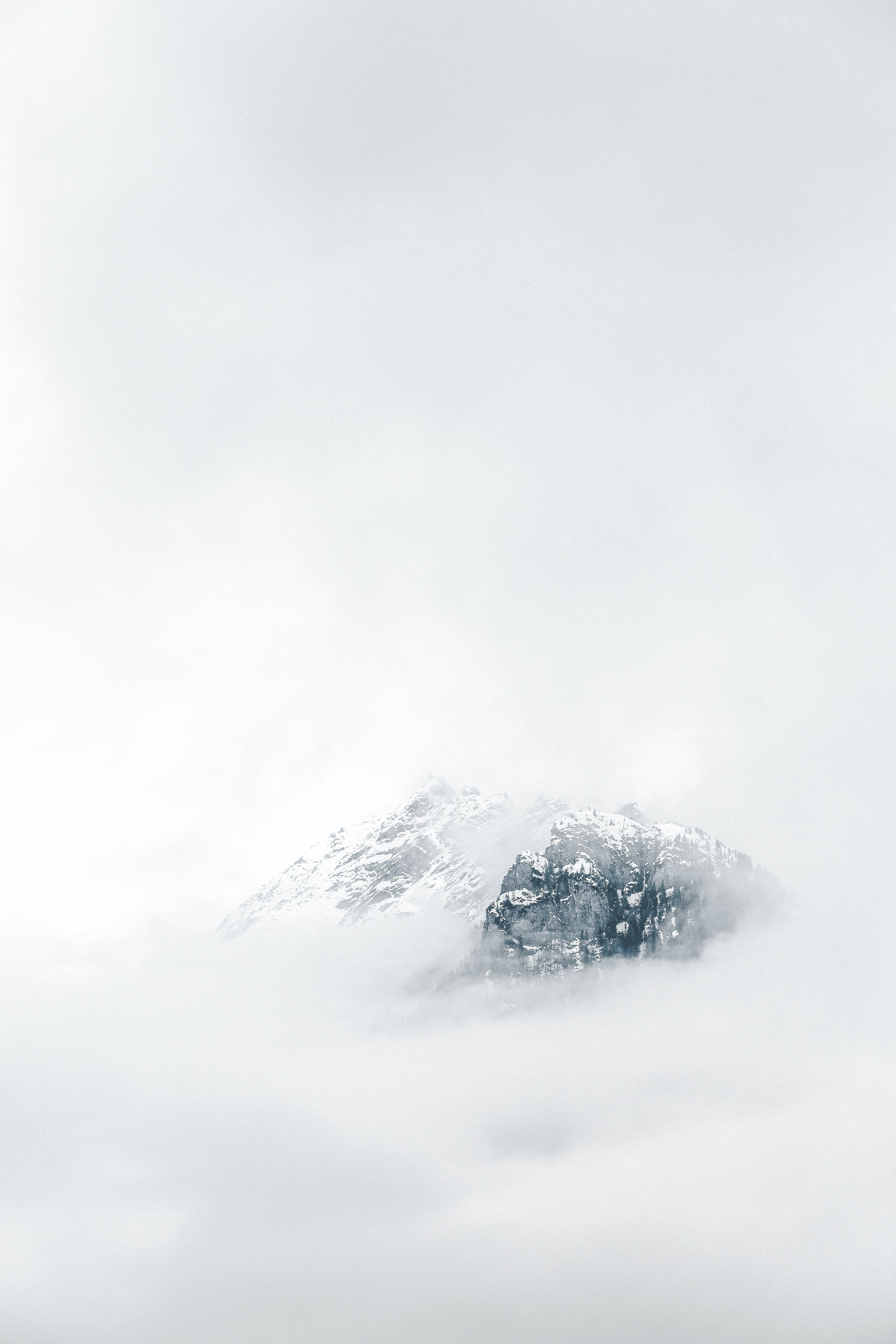 山景 桌布 壁紙 — 一個積雪的山峰從厚厚的雲層中浮現，呈現寧靜的冬日景象。