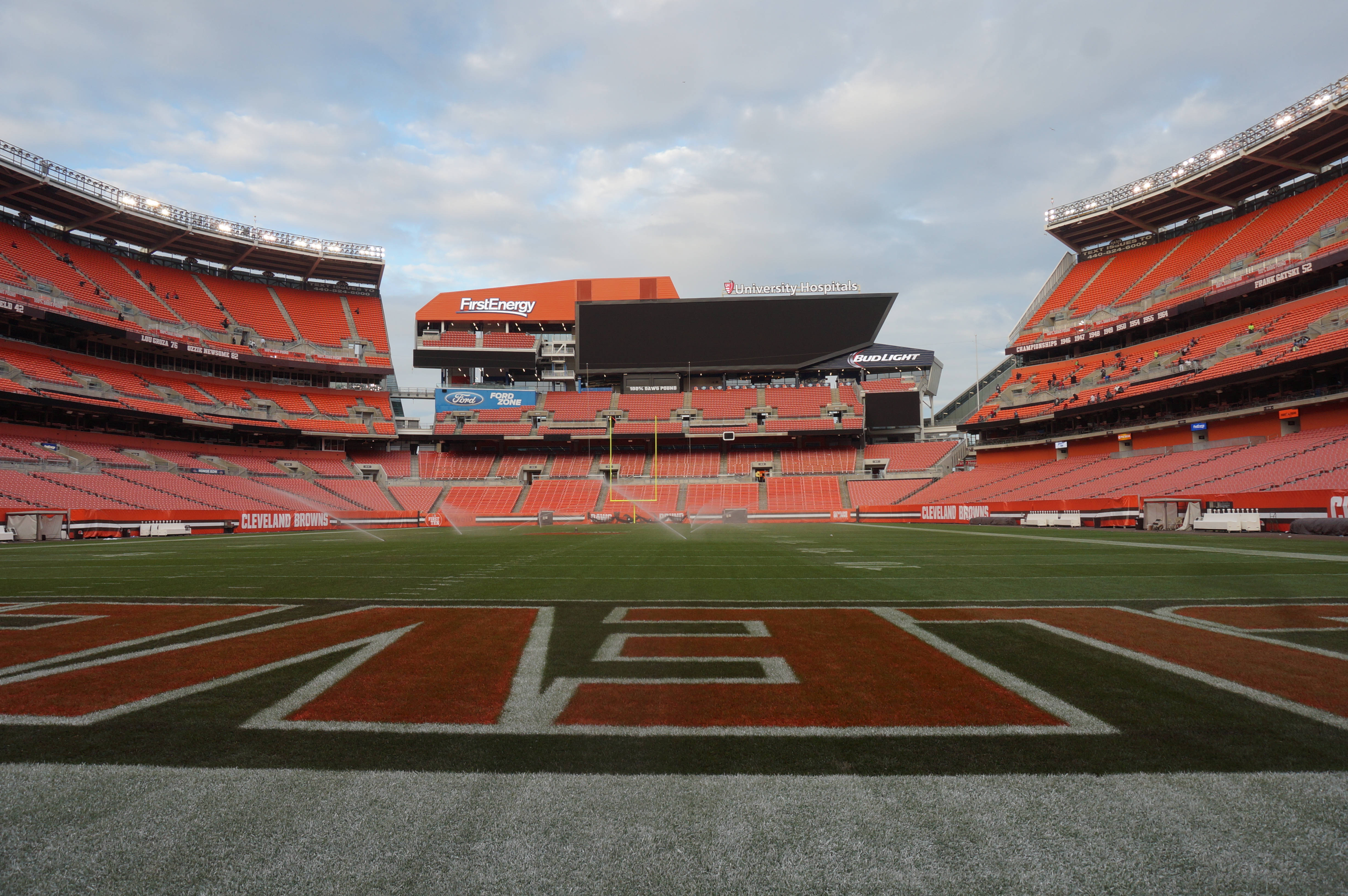 NFL 美式足球 桌布 壁紙 — 一個空無一人的克里夫蘭布朗體育場，設有橙色座位和綠色球場，天空多雲。