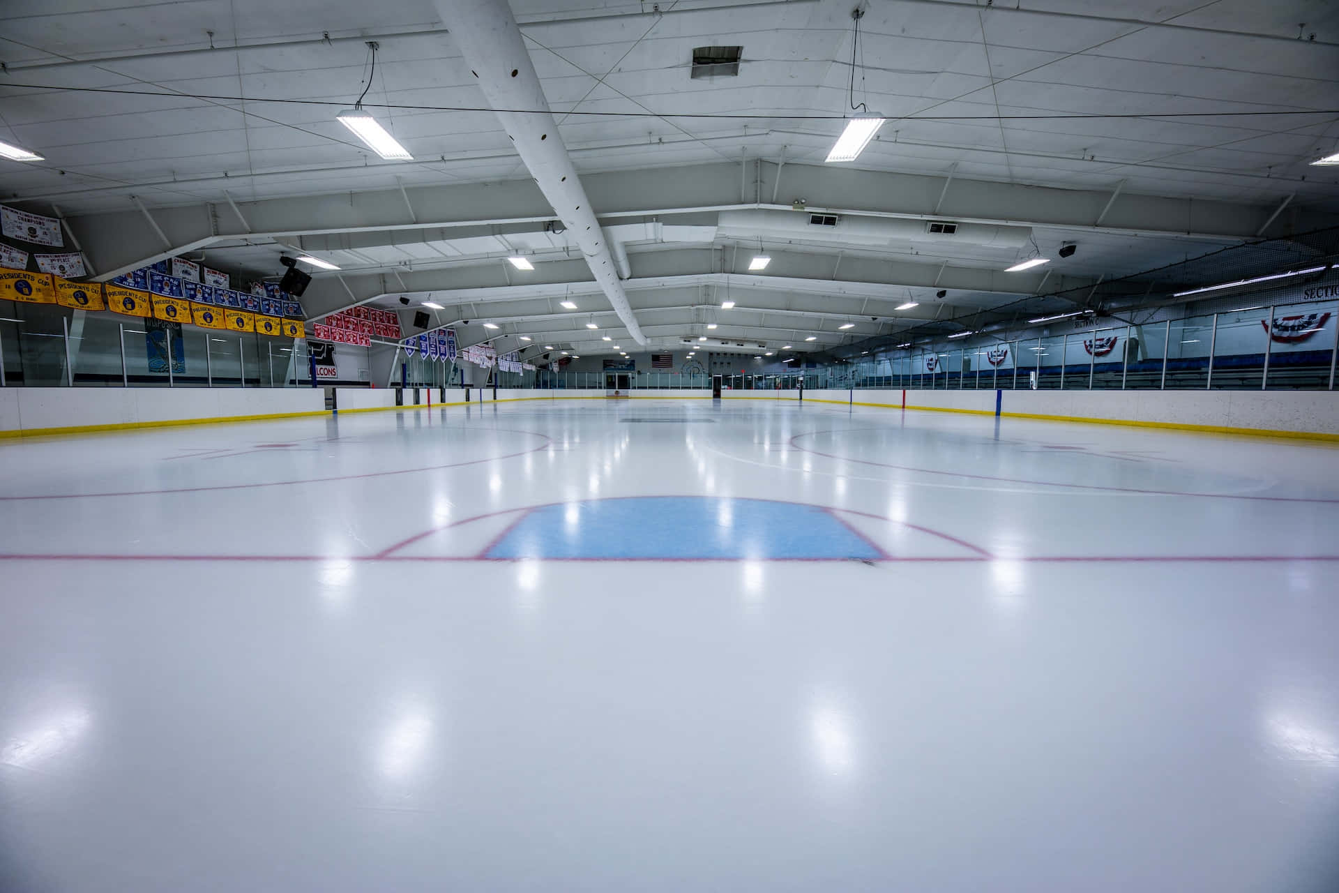 Ice Rink 桌布 壁紙 — 一個空無一物、潔淨的冰球場，上方有明亮的燈光，可見圍板和球門網。
