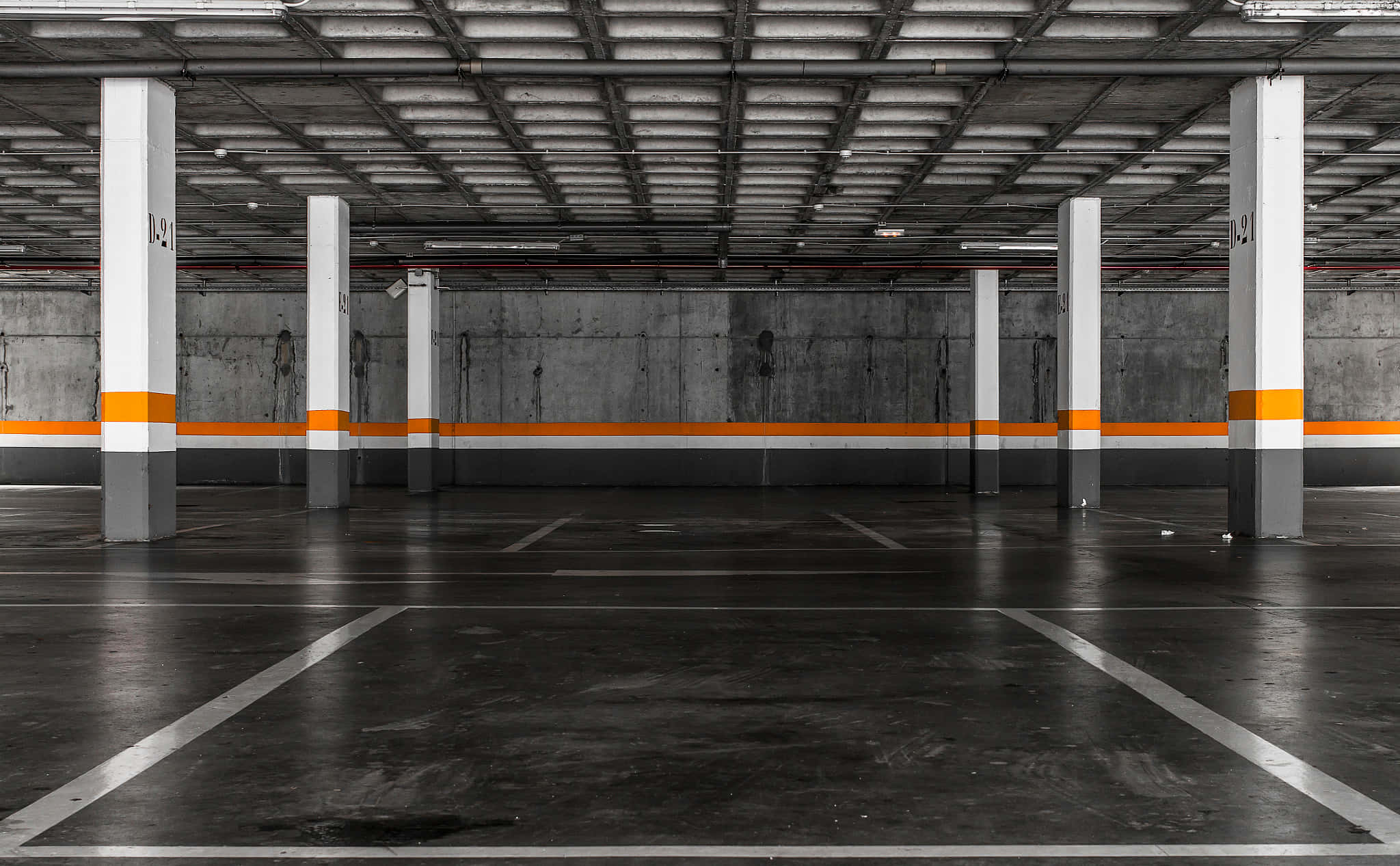 empty 桌布 壁紙 — 一個空置的地下停車場，混凝土柱上標有橙色帶和白色線條，地面為深色。