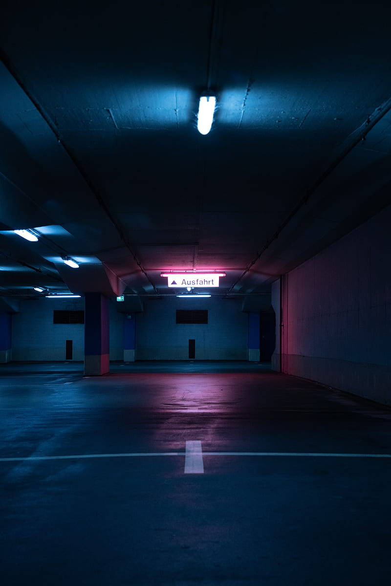 tunnel 桌布 壁紙 — 一個空蕩蕩的地下停車場，被天花燈具和遠處出口標誌的冷藍色和鮮豔粉紅色霓虹燈光所沐浴。