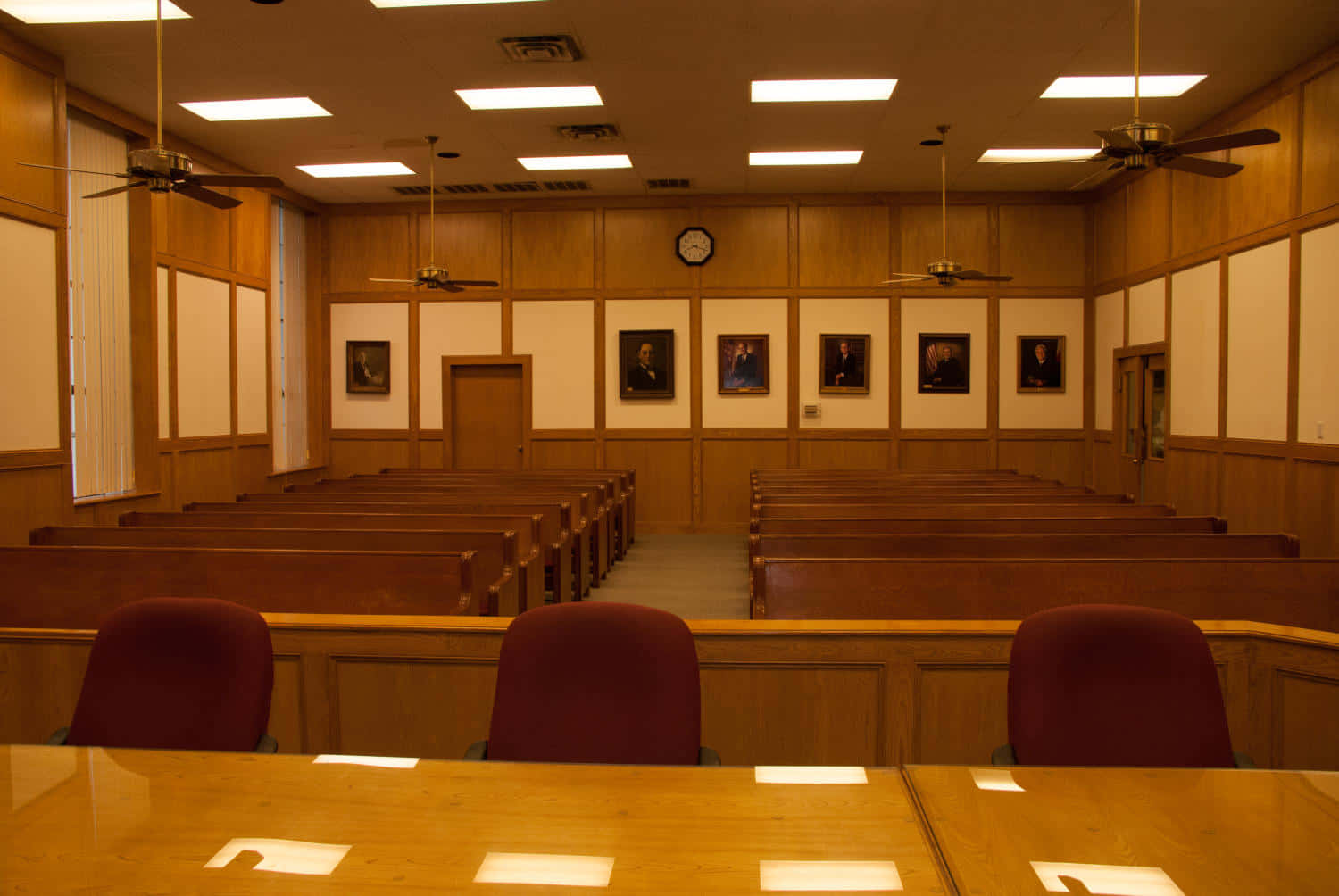 Court 桌布 壁紙 — 一個空蕩蕩的木製法庭，排排長凳，牆上掛著肖像畫，螢光燈下天花風扇轉動。