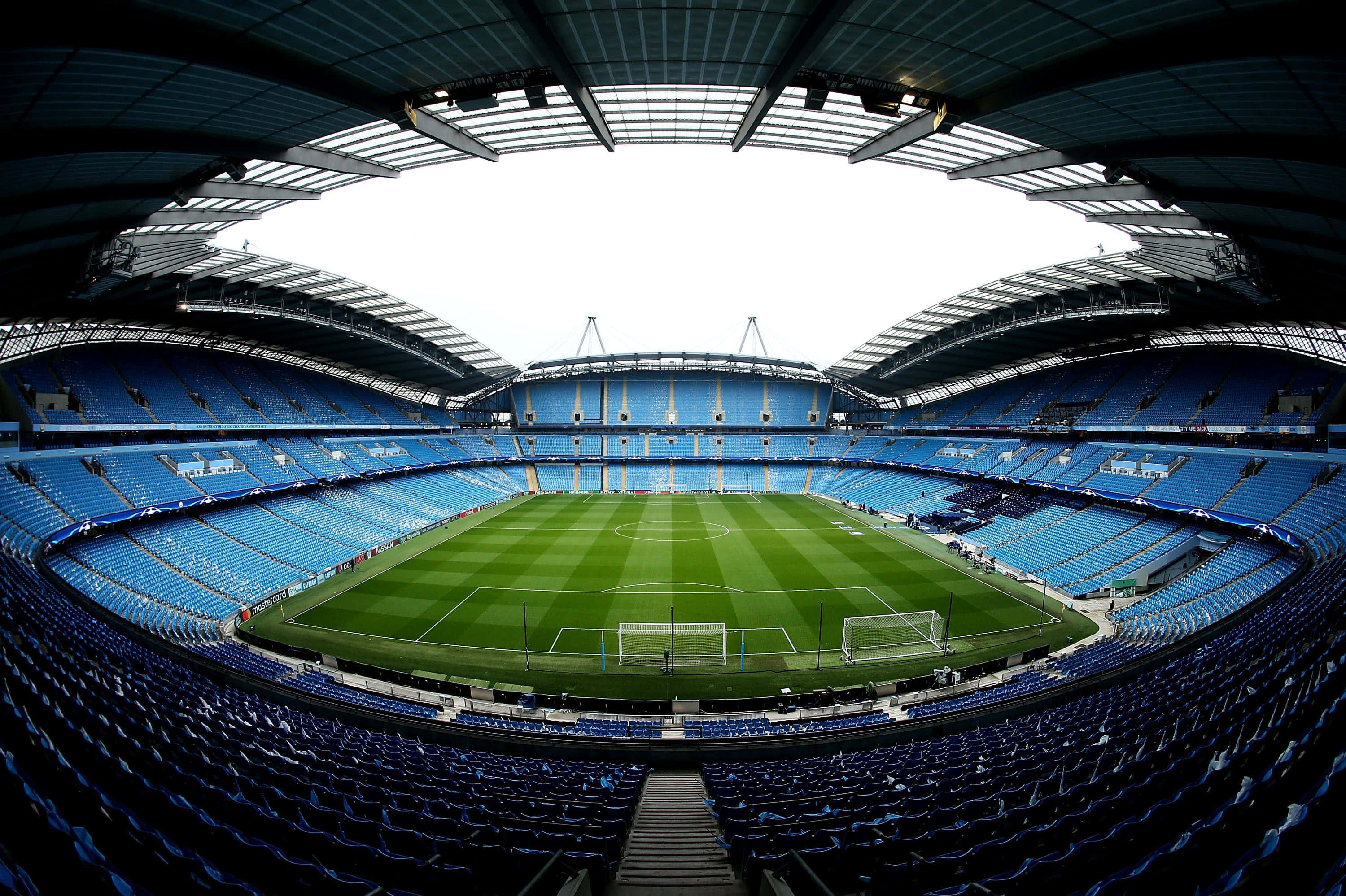 Soccer Stadium 桌布 壁紙 — 一個空蕩蕩的足球場的魚眼視角，藍色座位環繞著充滿活力的綠色球場，上方是開放式屋頂。