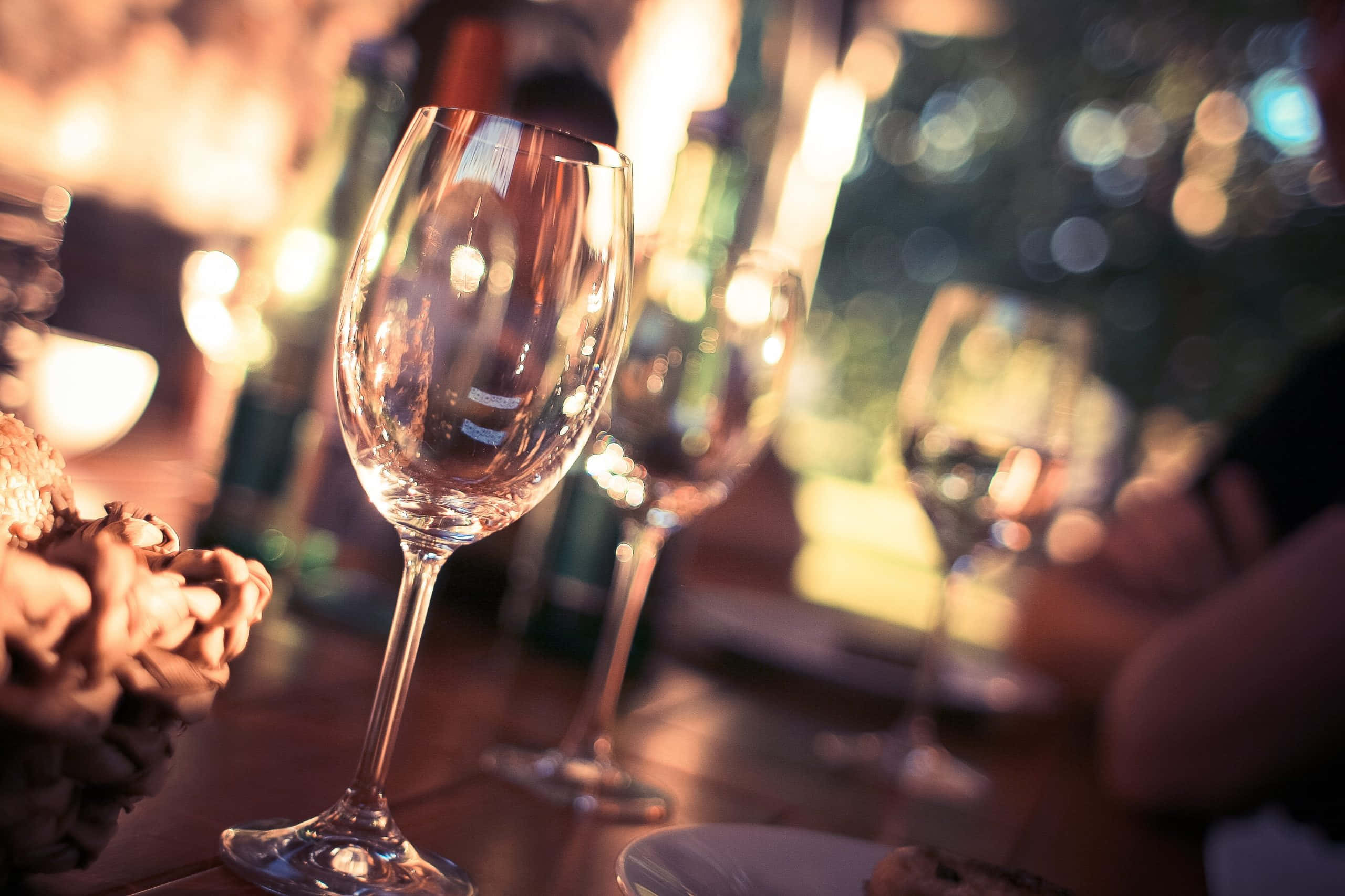 Wine Glass 桌布 壁紙 — 一個空酒杯的特寫，放在燈光昏暗的桌子上，背景有模糊的散景燈光和一個人的手臂。